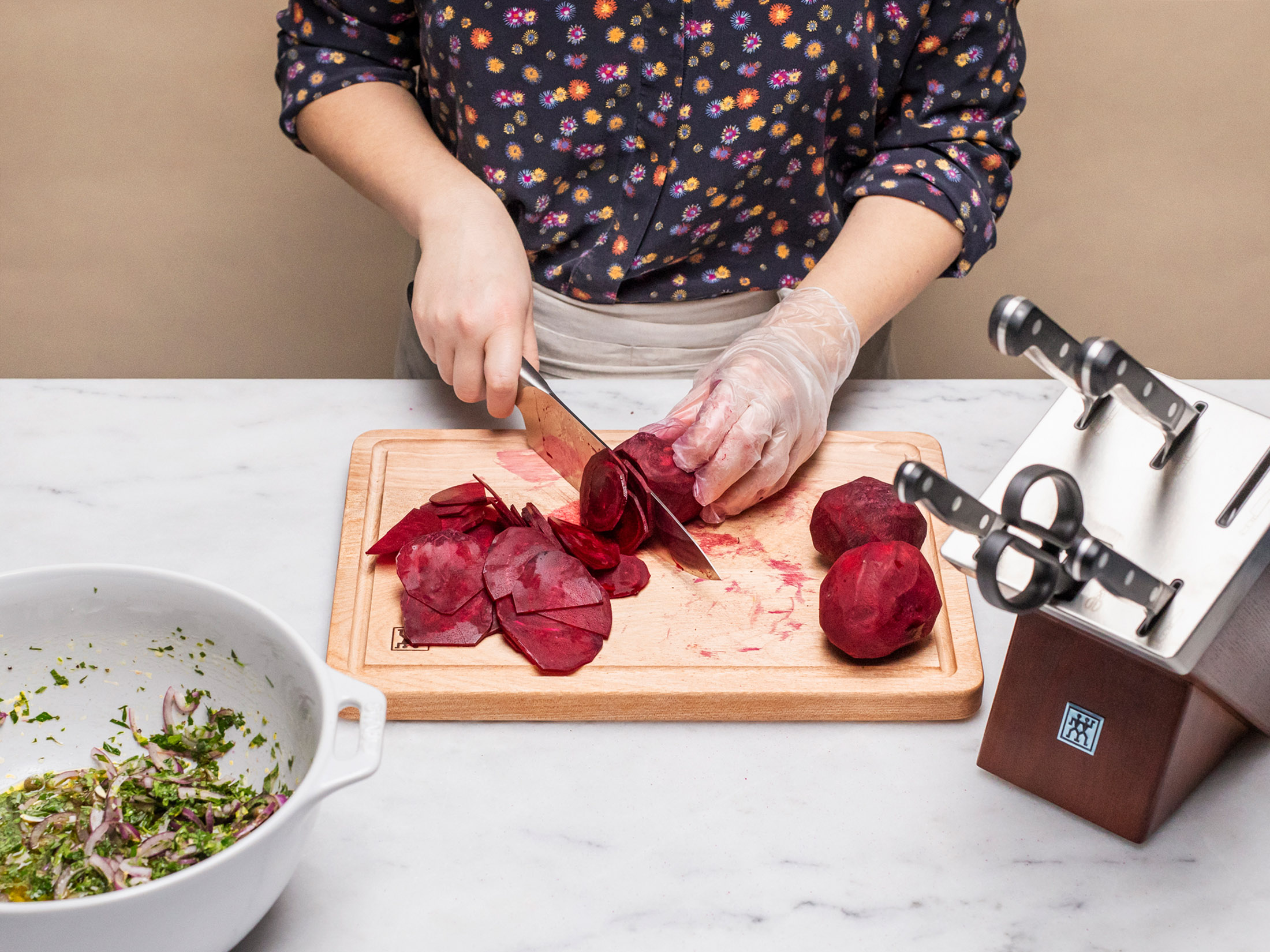 Una persona affetta barbabietole rosse su un tagliere di legno. Sono visibili anche barbabietole a fette, intere e una ciotola di insalata.