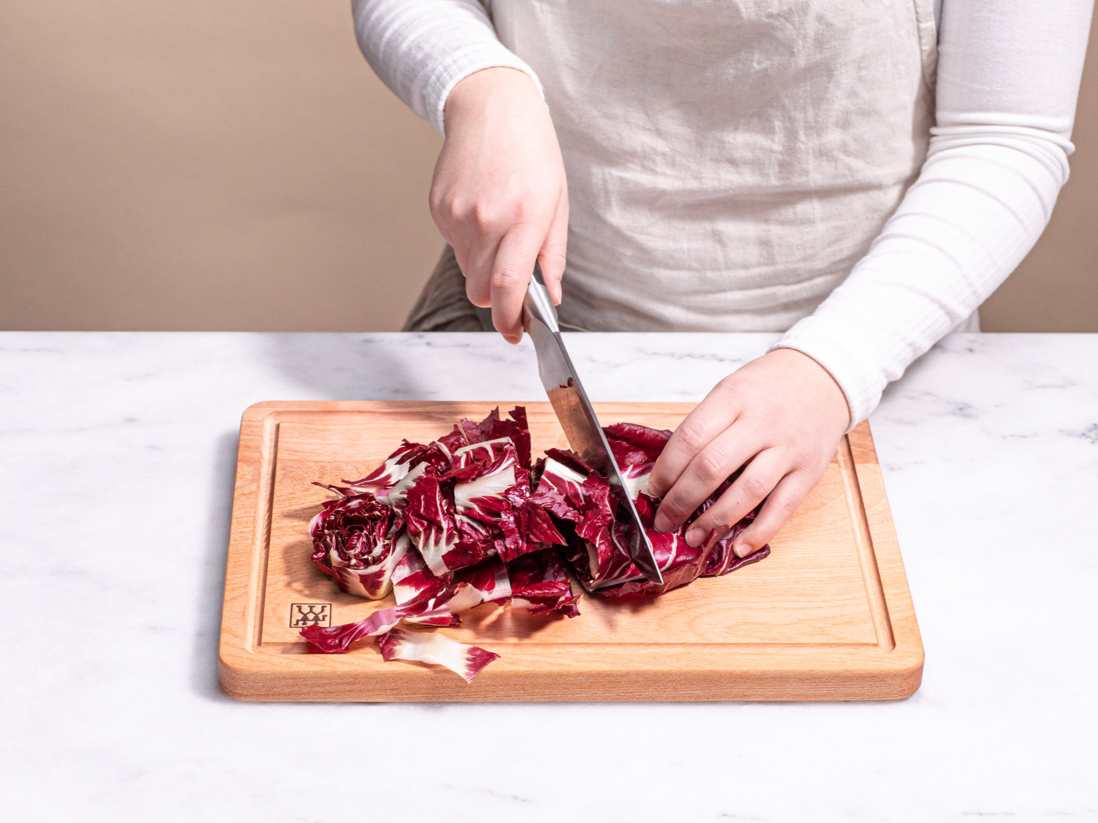 Una persona taglia radicchio rosso su un tagliere di legno con un coltello. Lo sfondo è neutro.