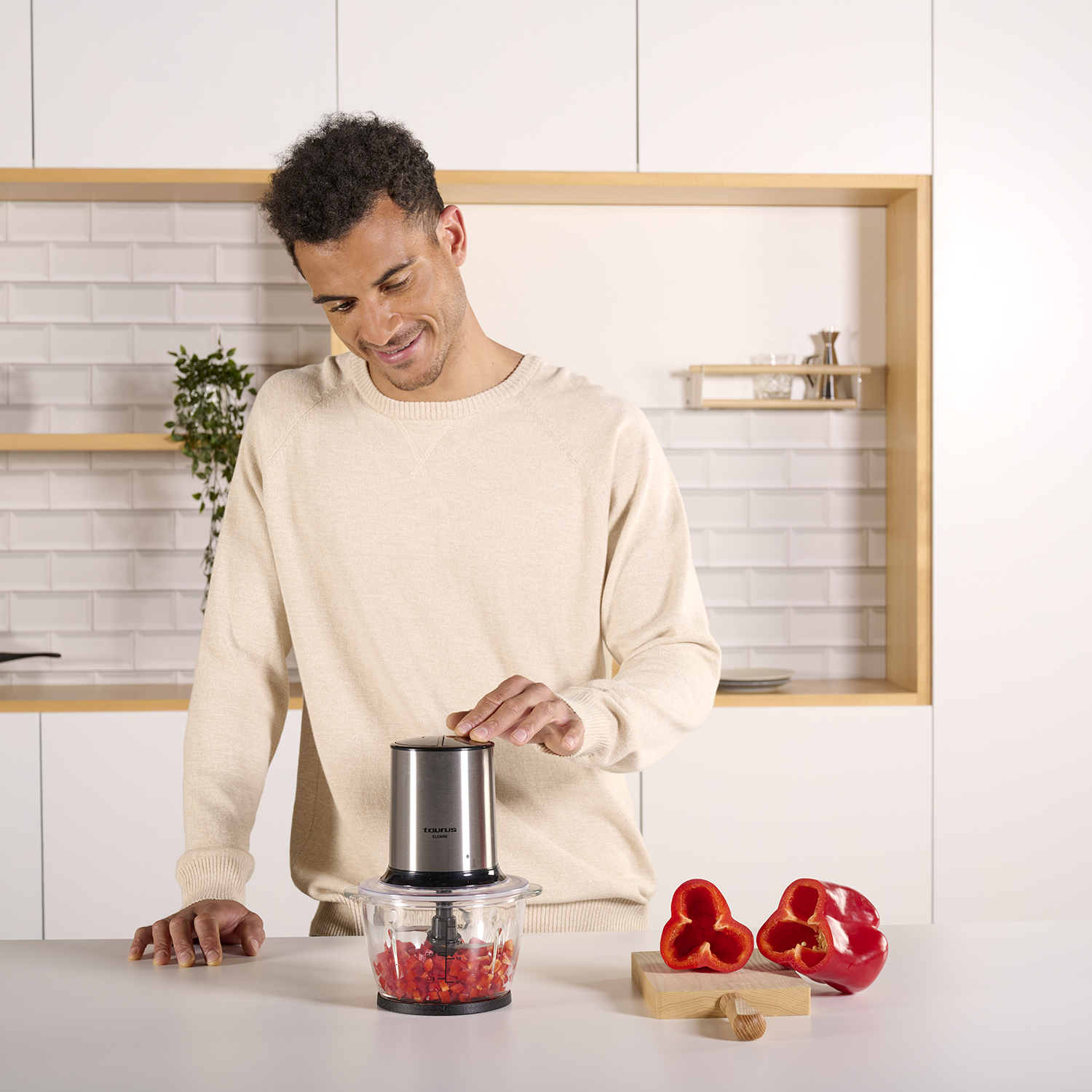 Un hombre usa un procesador de alimentos plateado y negro. Pimientos rojos en el mostrador.