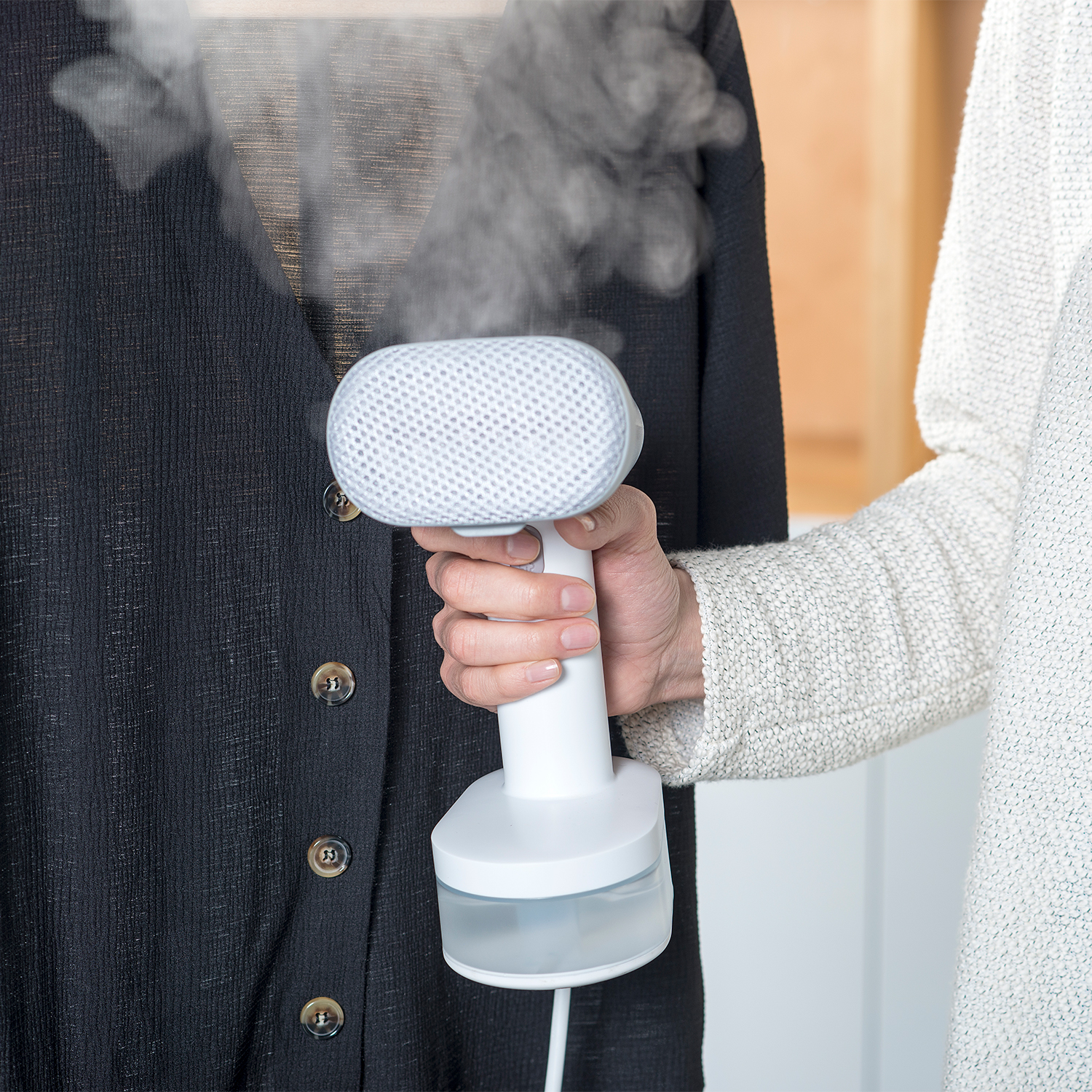 Eine Person bügelt ein schwarzes Hemd mit Knöpfen mit einem weißen Handdampfer, Dampf steigt auf.