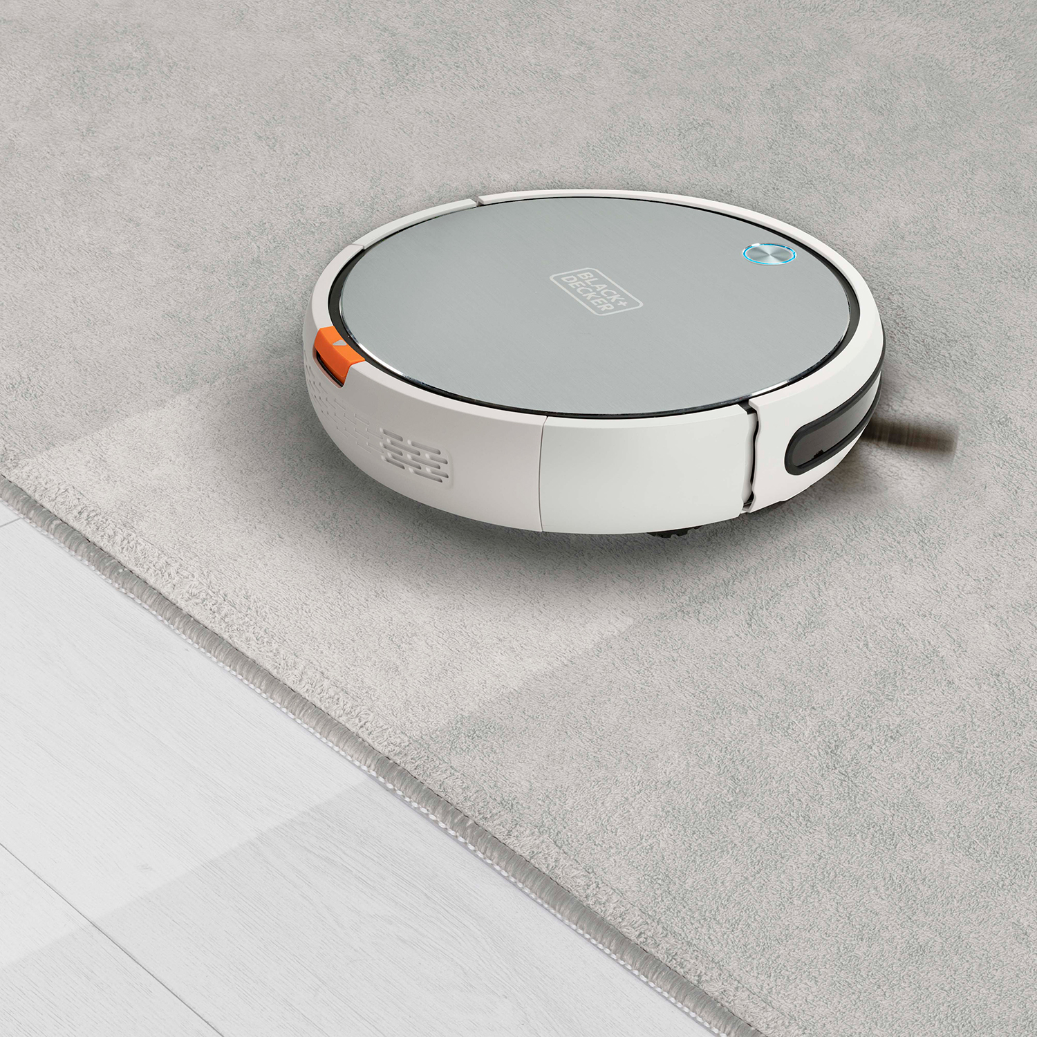 Biało-szary robot odkurzający na szarej wykładzinie.