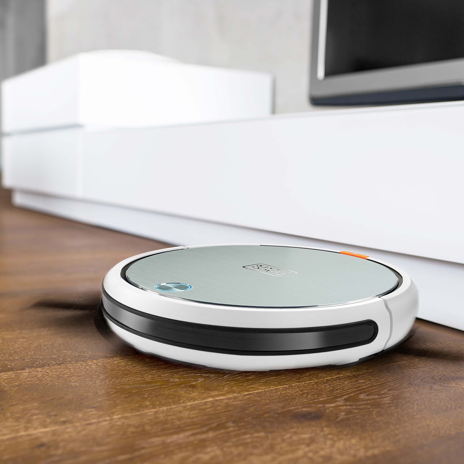 Okrągły, srebrno-czarny odkurzacz robot na drewnianej podłodze.