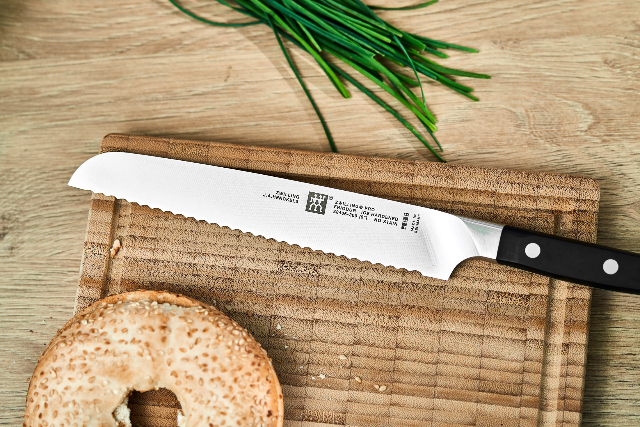 Nóż do chleba i bajgiel na drewnianej desce do krojenia. Szczypiorek w tle.