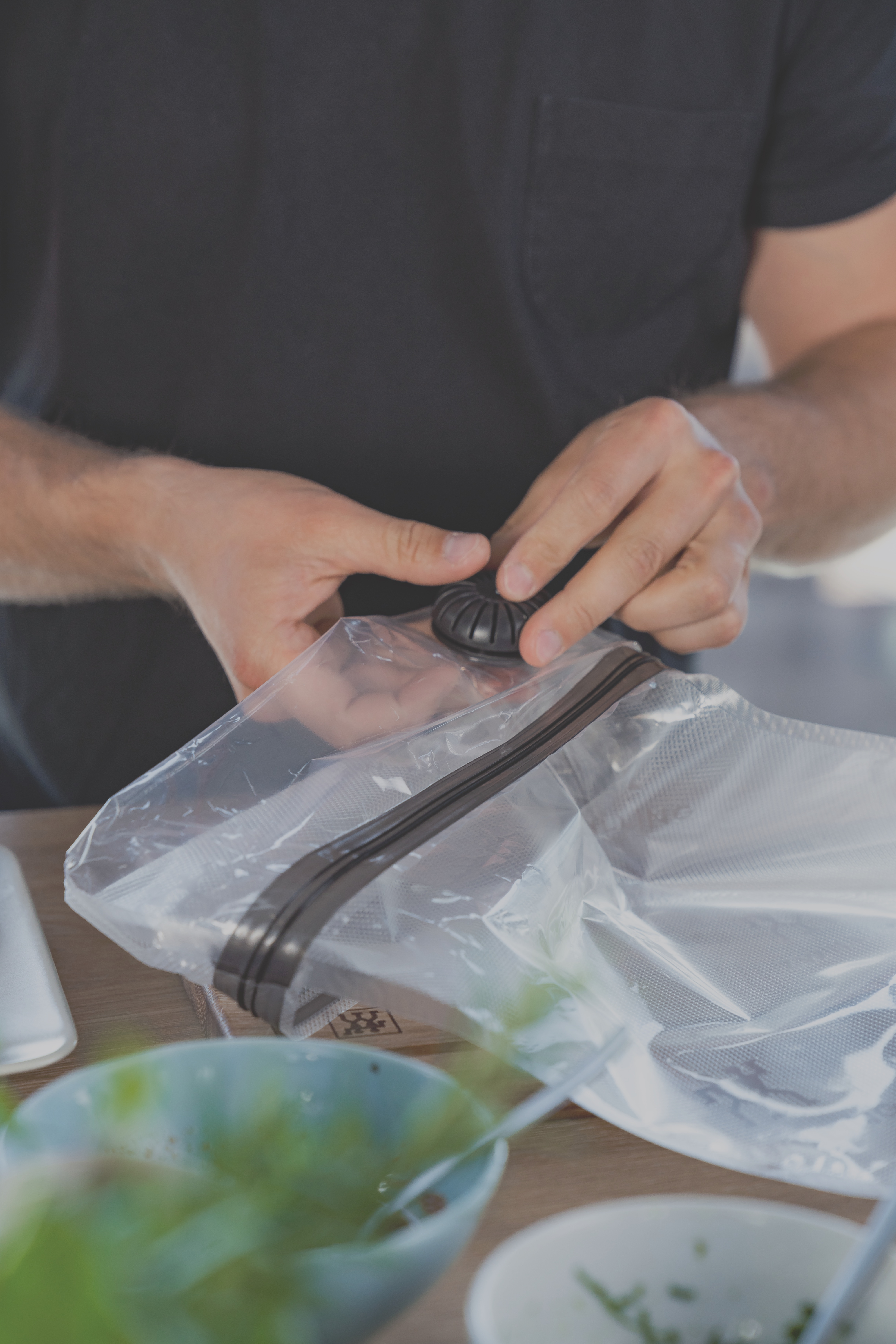 Persona usando sellador al vacío en bolsa transparente, con cuencos en el fondo.