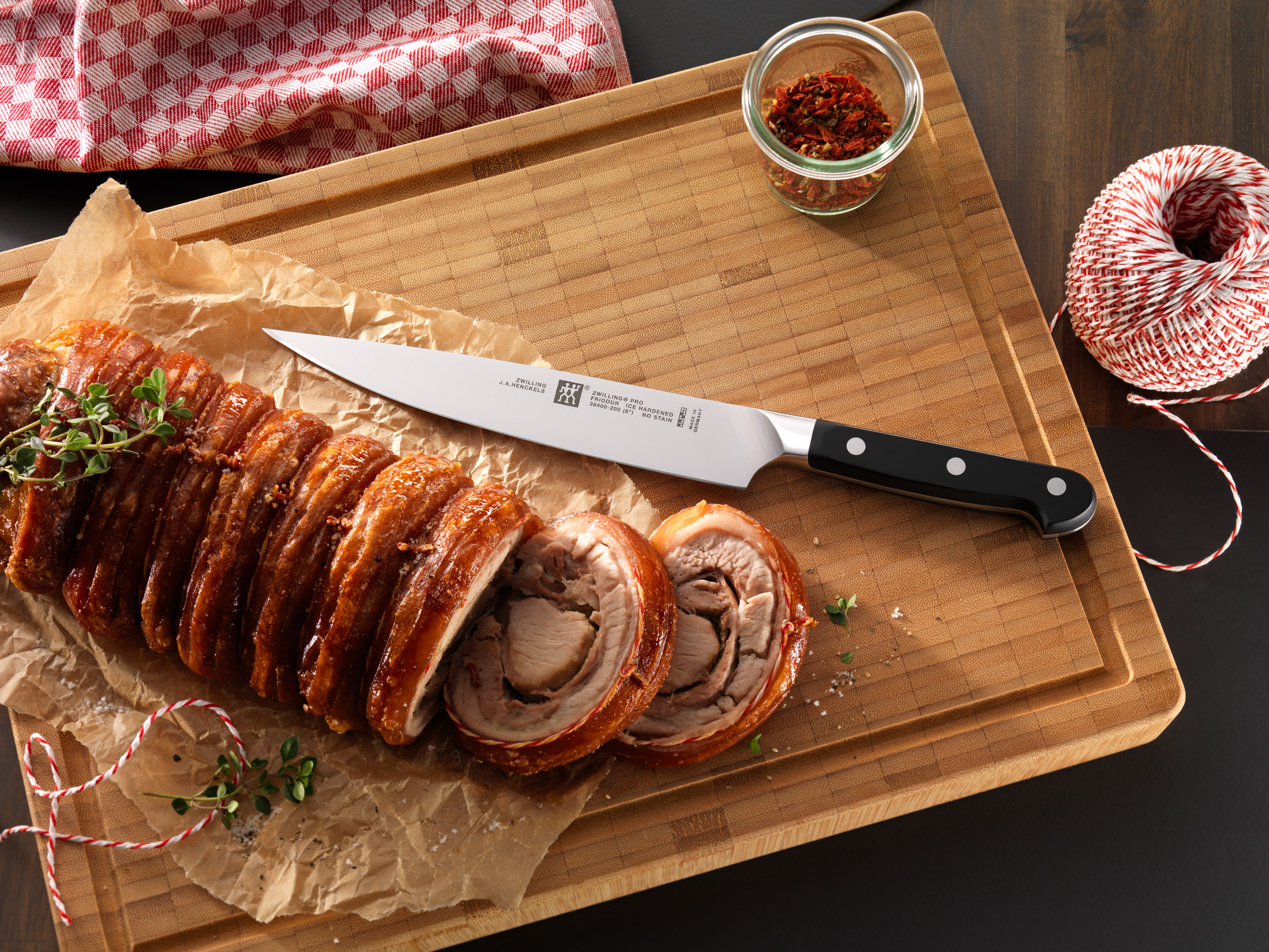 Kompozycja potraw na drewnianej desce: krojona rolada mięsna, nóż, przyprawy, sznurek. Ciemne tło.