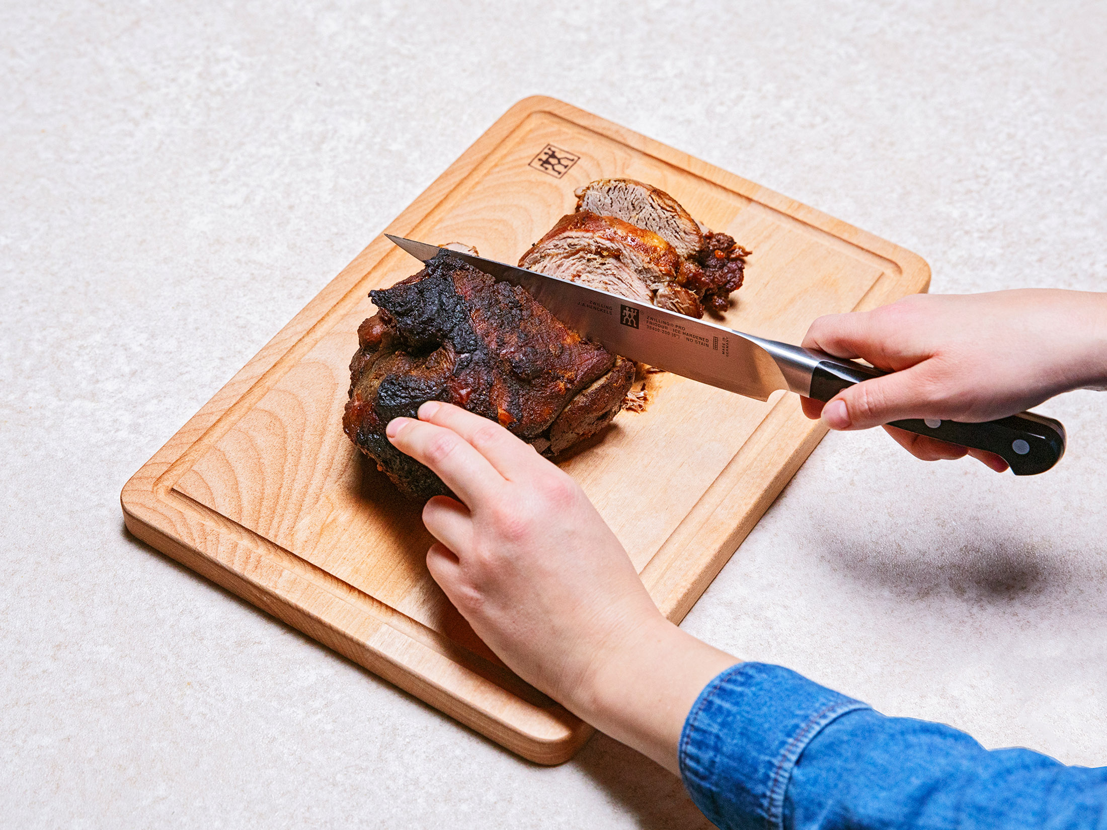 Ręce krojące pieczone mięso na drewnianej desce do krojenia nożem szefa kuchni, ujęcie z bliska.