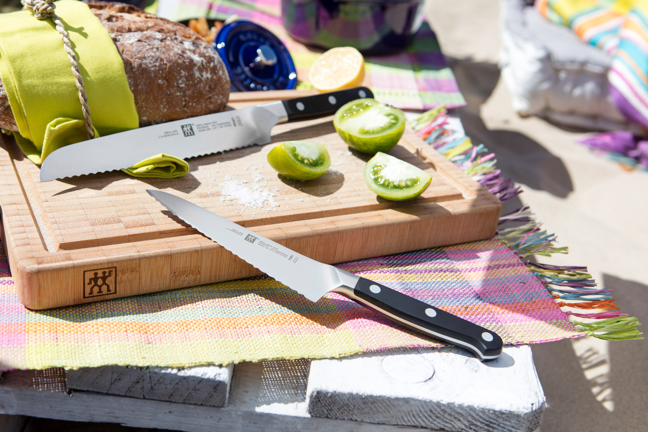 Chleb, pomidory i noże na drewnianej desce do krojenia. Sól i cytryna. Kolorowa tkana mata i piknik.