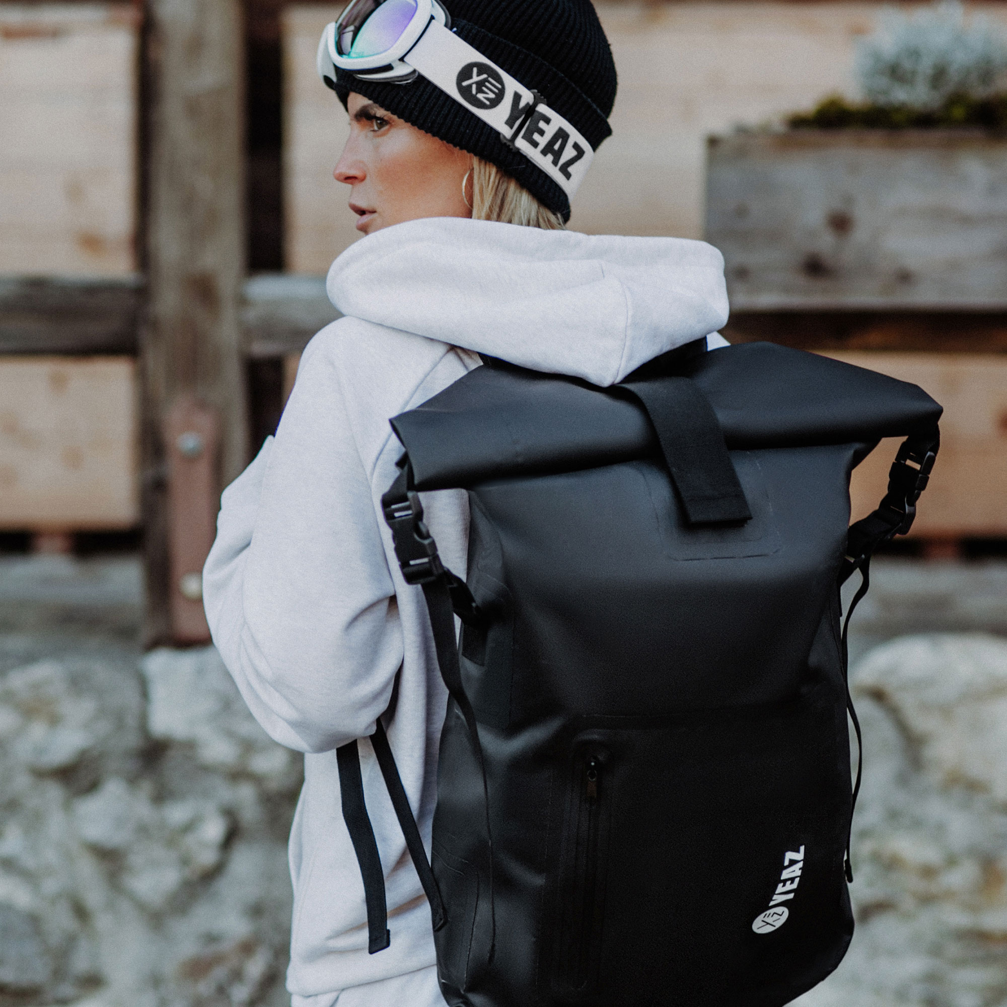 Eine Frau in einer Mütze und einer Brille mit einem schwarzen Rucksack. Sie ist vom Betrachter abgewandt.