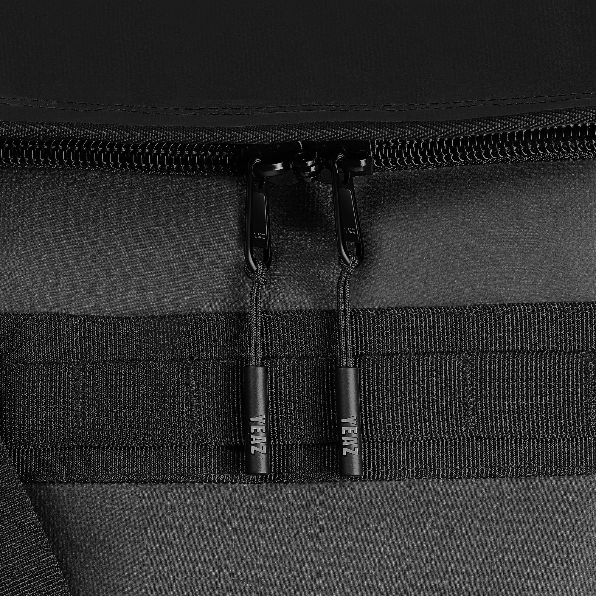 Schwarze Tasche mit zwei Reißverschlüssen und schwarzen Riemen. Die Reißverschlüsse haben kleine VEAZ-Anhänger.