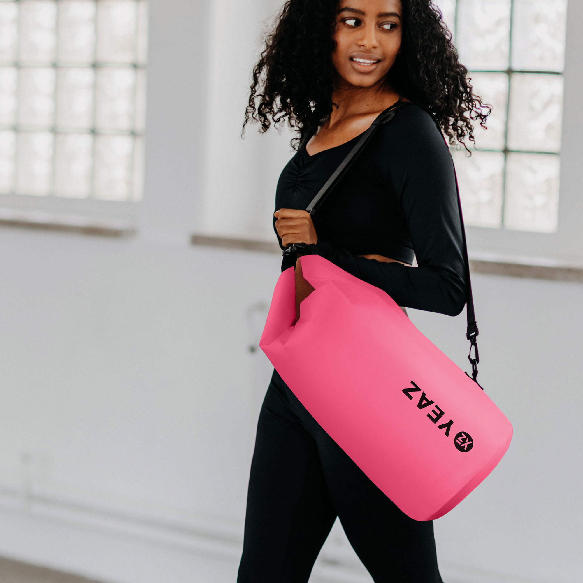 Una mujer con ropa deportiva negra lleva una bolsa de lona rosa brillante con una correa negra.