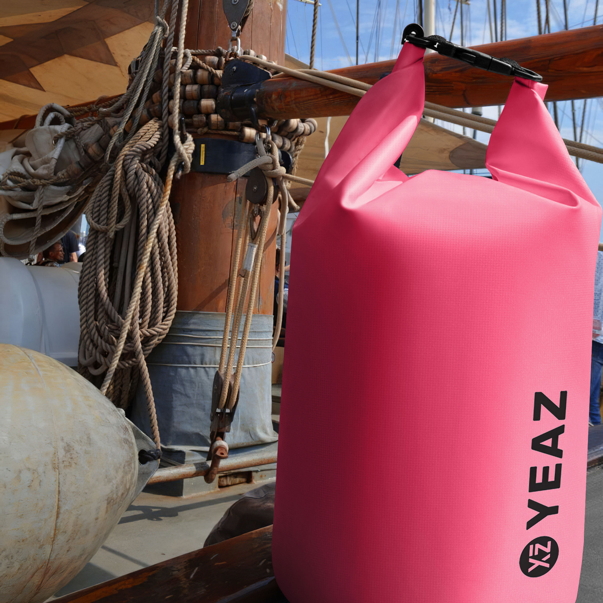 Una bolsa impermeable rosa colgada en un barco, con cuerdas y madera visibles.