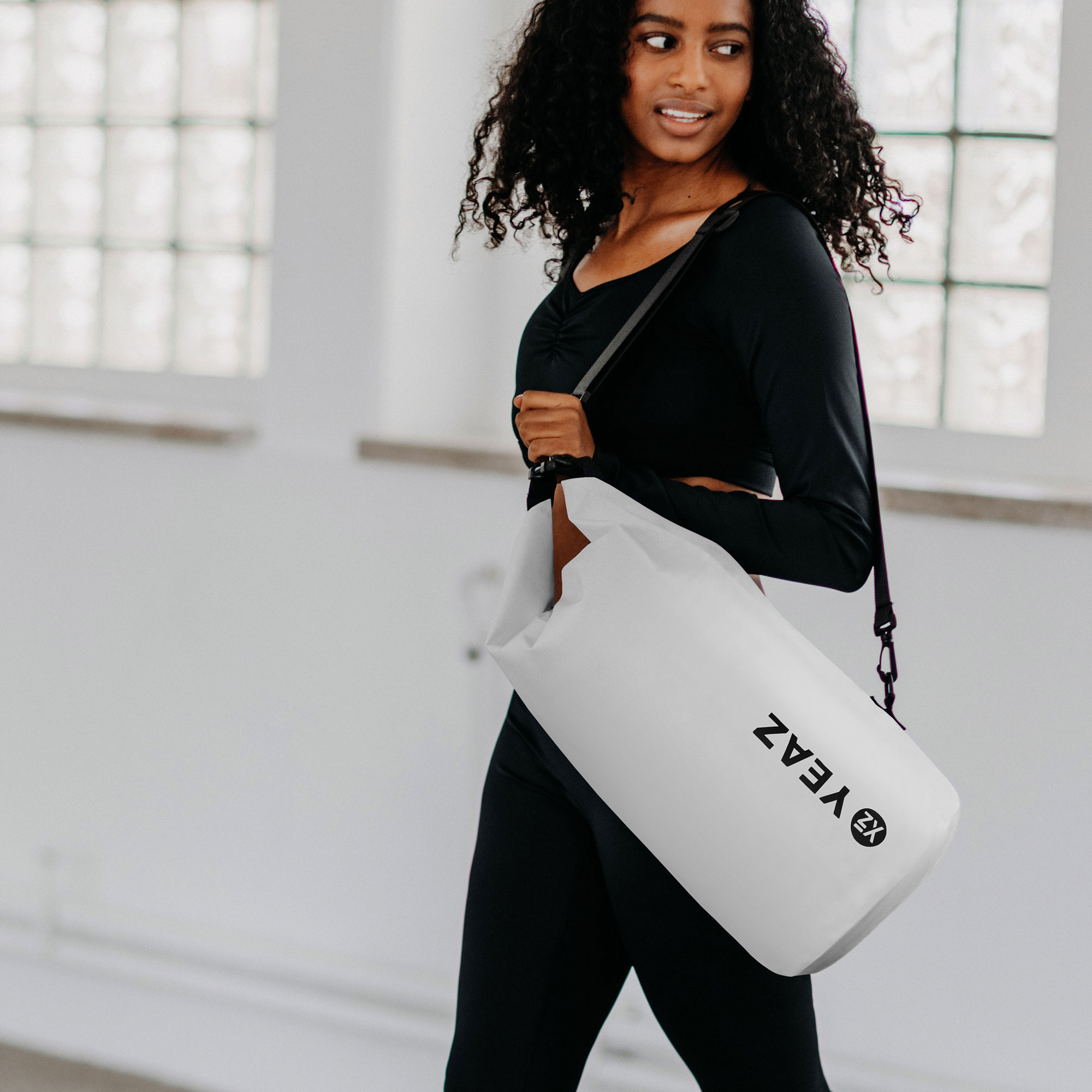Mujer con bolso blanco. Viste leggins negros y manga larga negra.