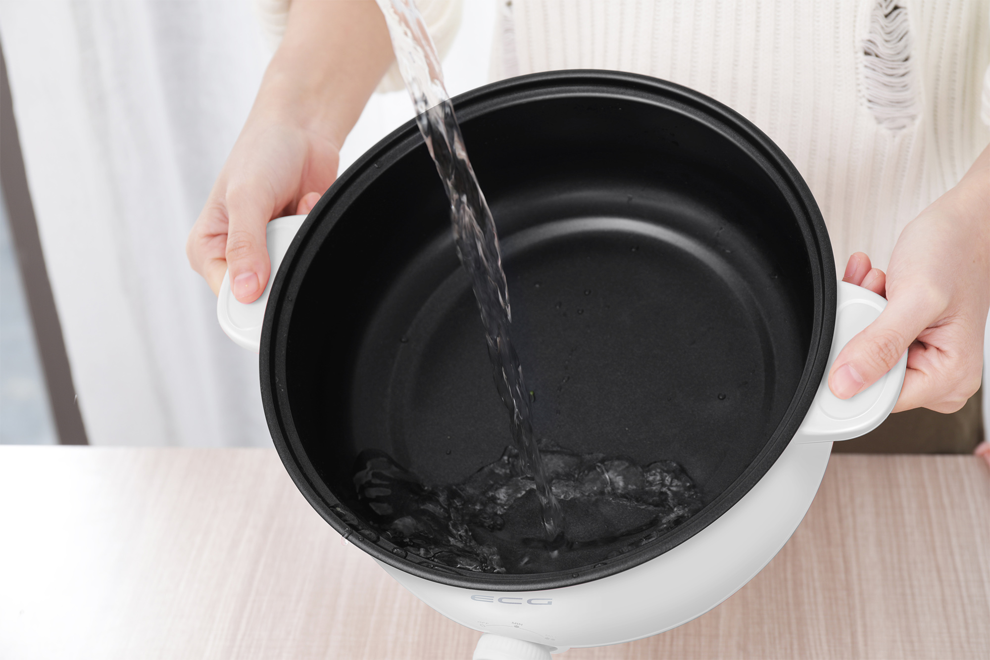 Hände gießen Wasser in eine weiße Pfanne.