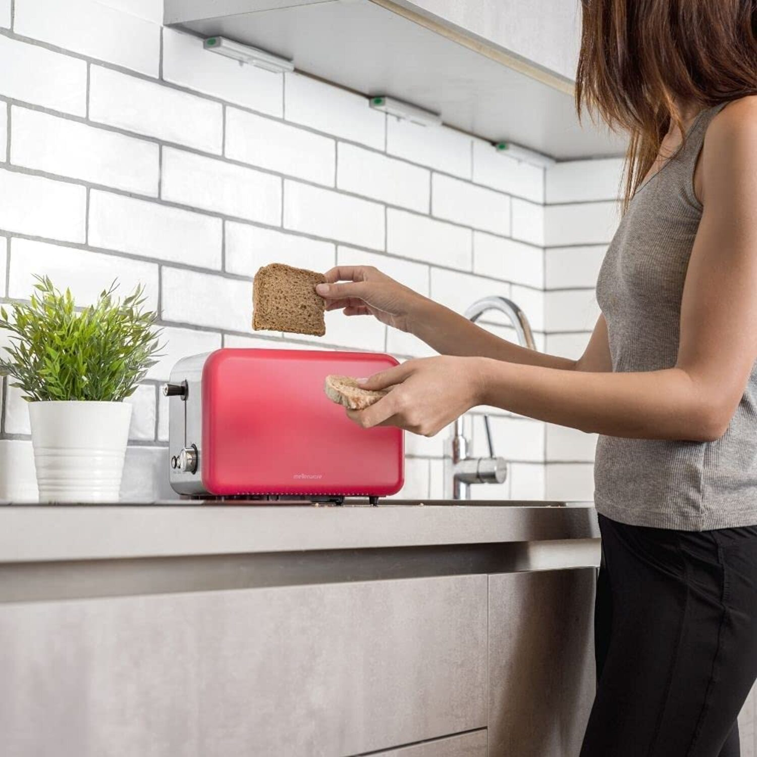 Una mujer sosteniendo tostadas cerca de una tostadora roja en una cocina. Una planta está en la encimera.