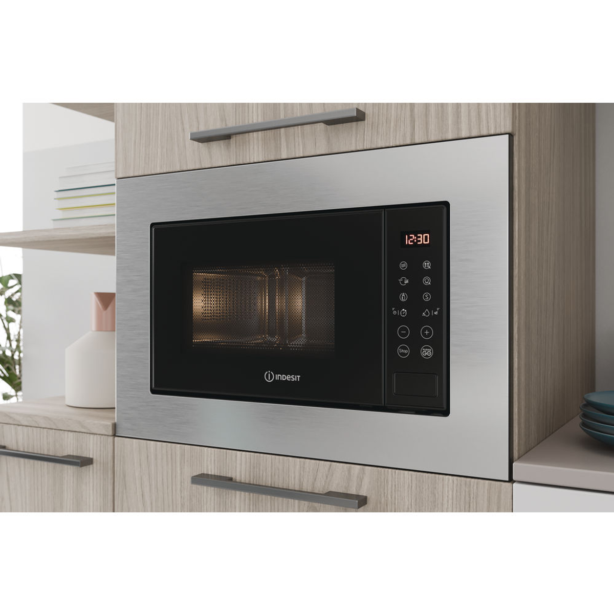 Un microondas Indesit empotrado, marco plateado, en un mueble de madera.