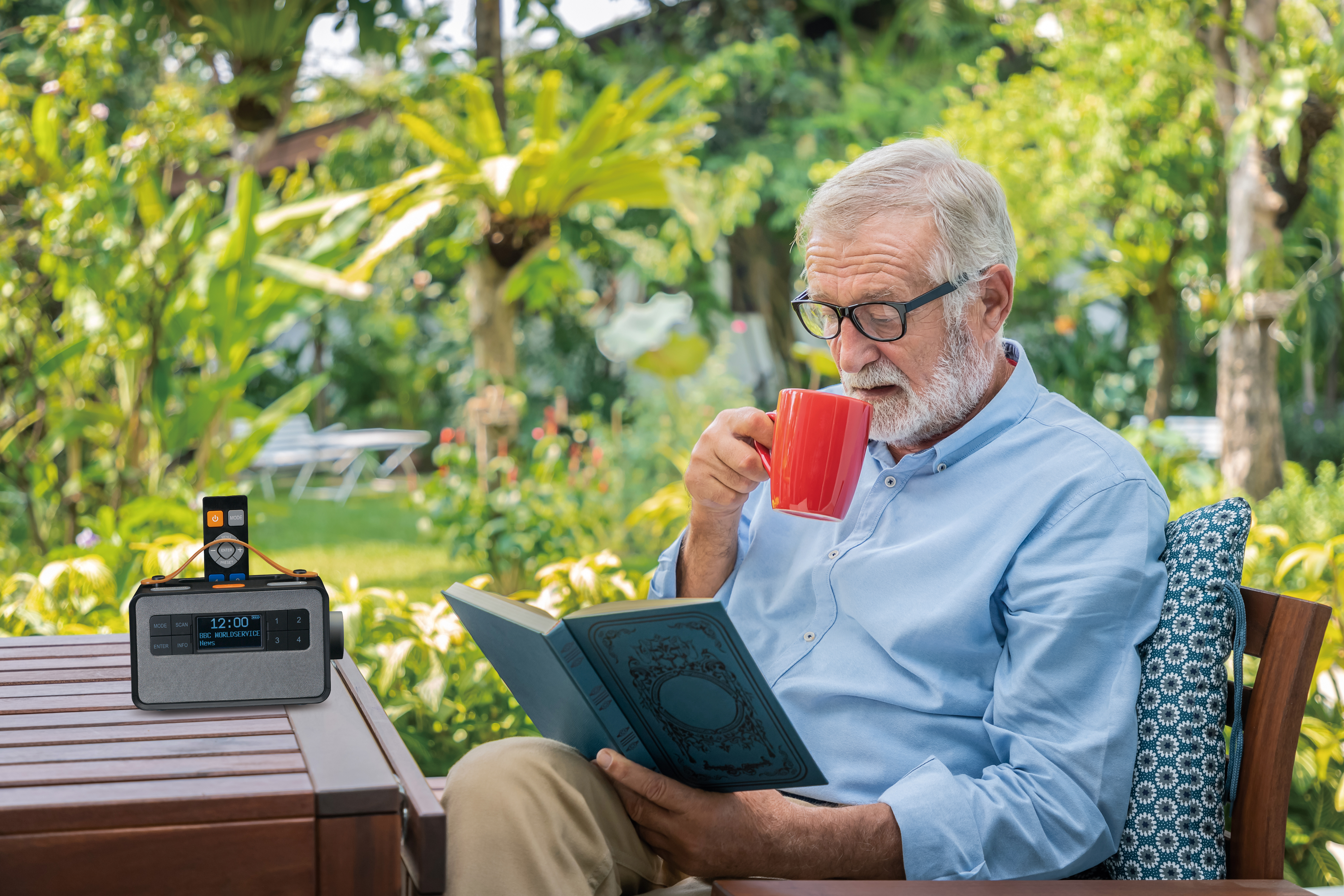 Starszy mężczyzna pijący z czerwonego kubka podczas czytania książki, obok radia.