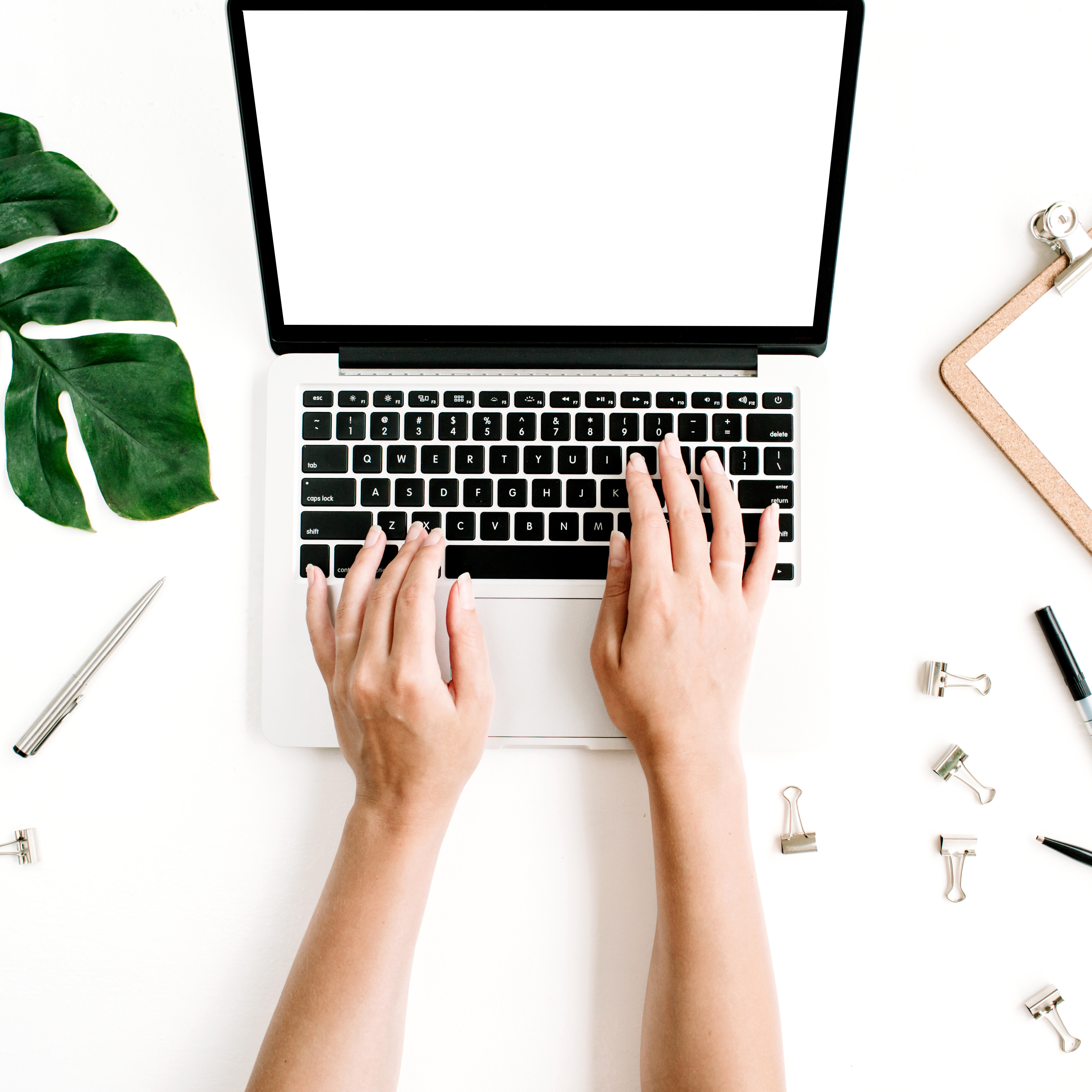 Laptop mit Händen, die auf der Tastatur tippen, ein Blatt und Bürobedarf auf einem weißen Schreibtisch.