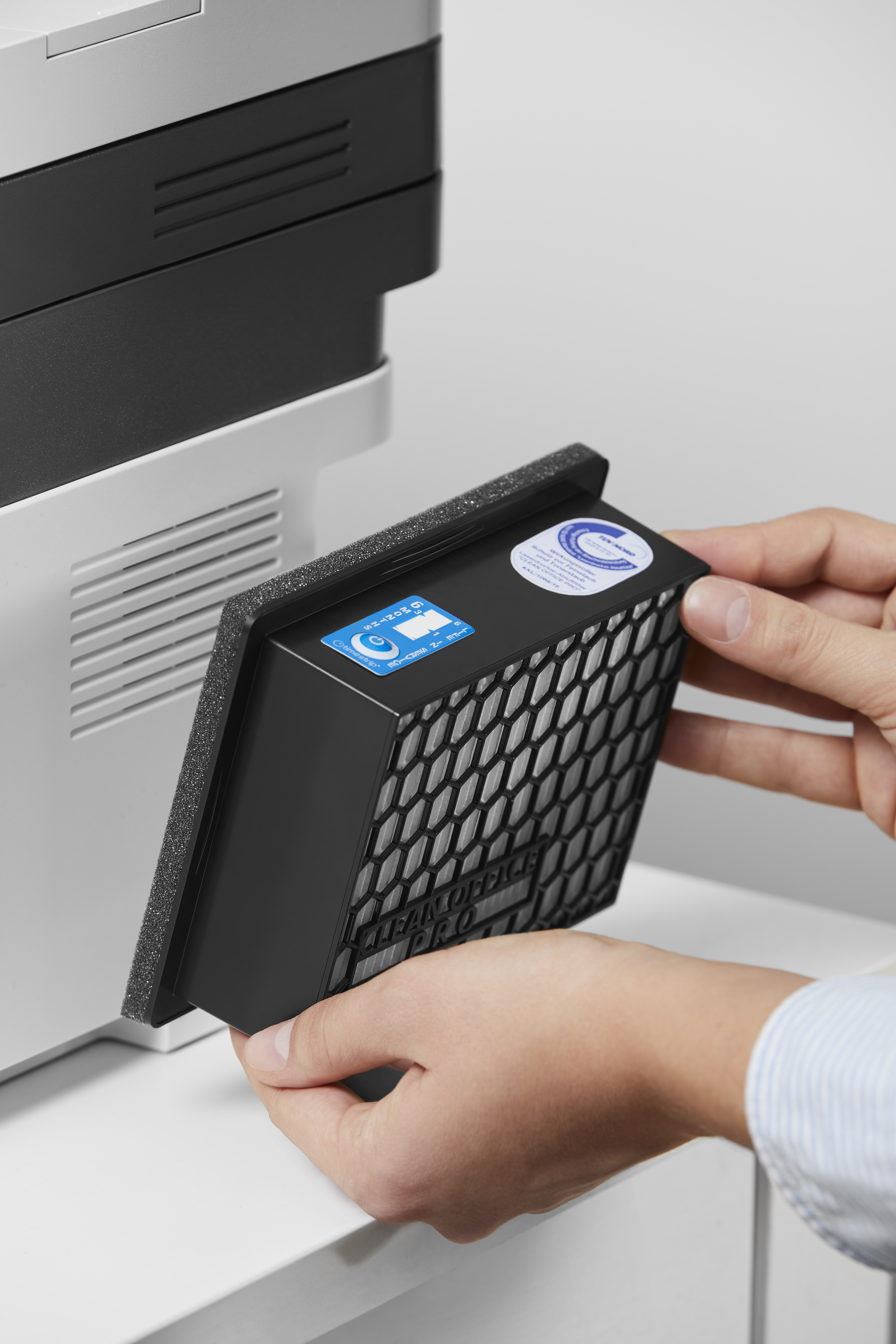 Osoba instalująca czarny filtr w drukarce, zbliżenie na dłonie i filtr.