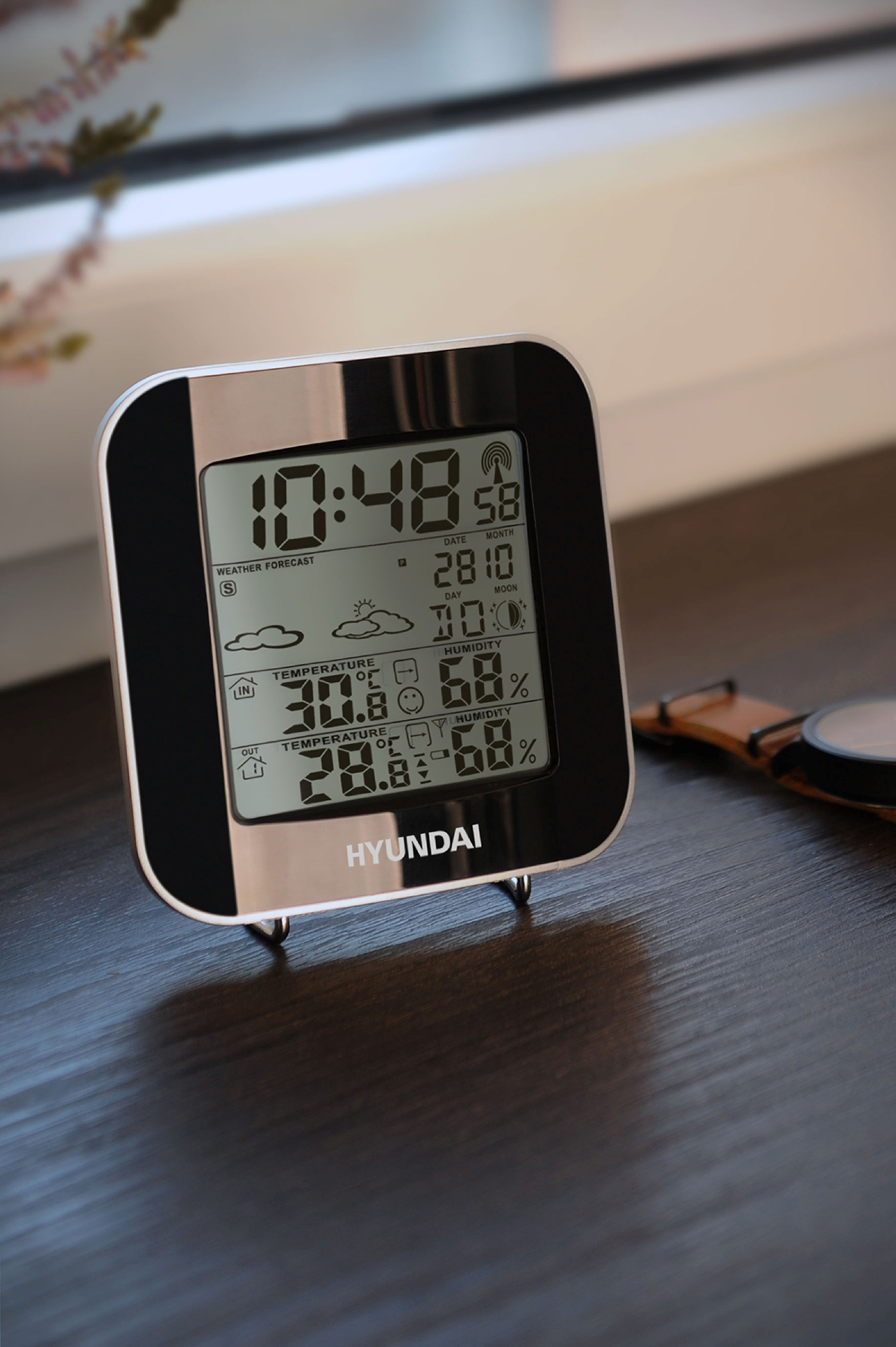 Digitale Wetterstation mit Uhrzeit, Datum und Wetterdetails. Es steht auf einer dunklen Oberfläche.