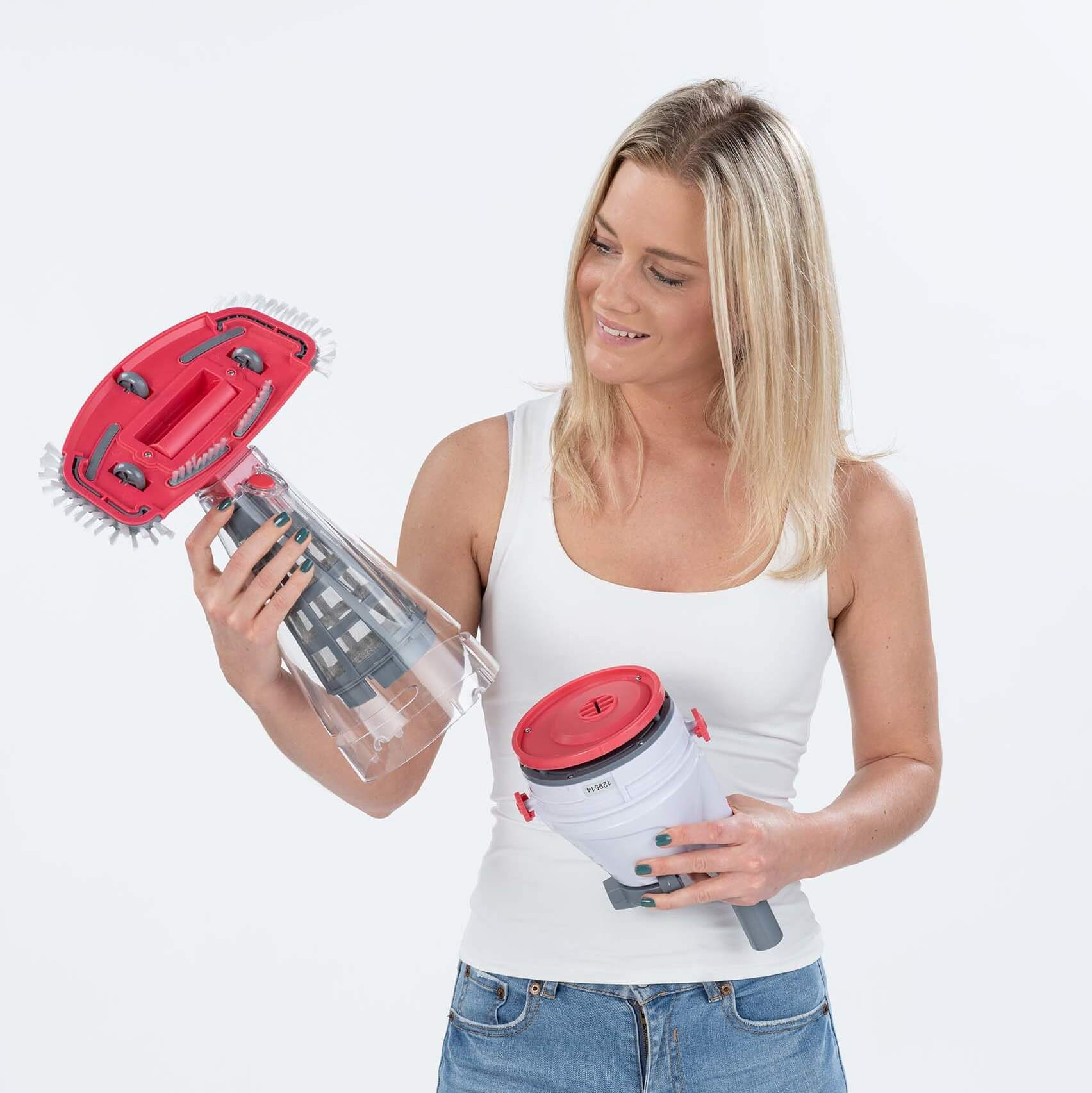 Eine Frau hält zwei Teile eines Staubsaugers und lächelt in die Kamera.