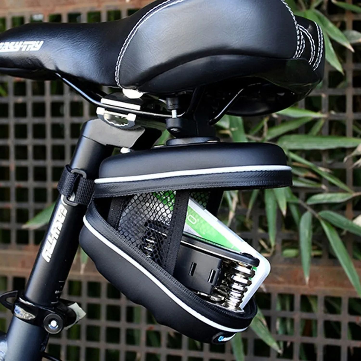 Ein schwarzer Fahrradsattel mit einer schwarzen Tasche befindet sich an einem Fahrrad. Die Tasche ist offen und enthält Werkzeug.