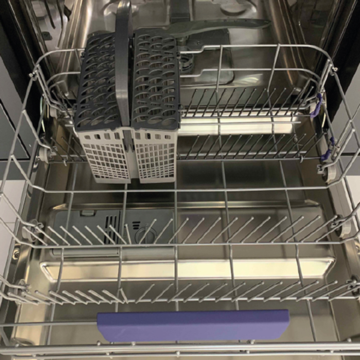 Interior de un lavavajillas con rejillas y un soporte para utensilios.
