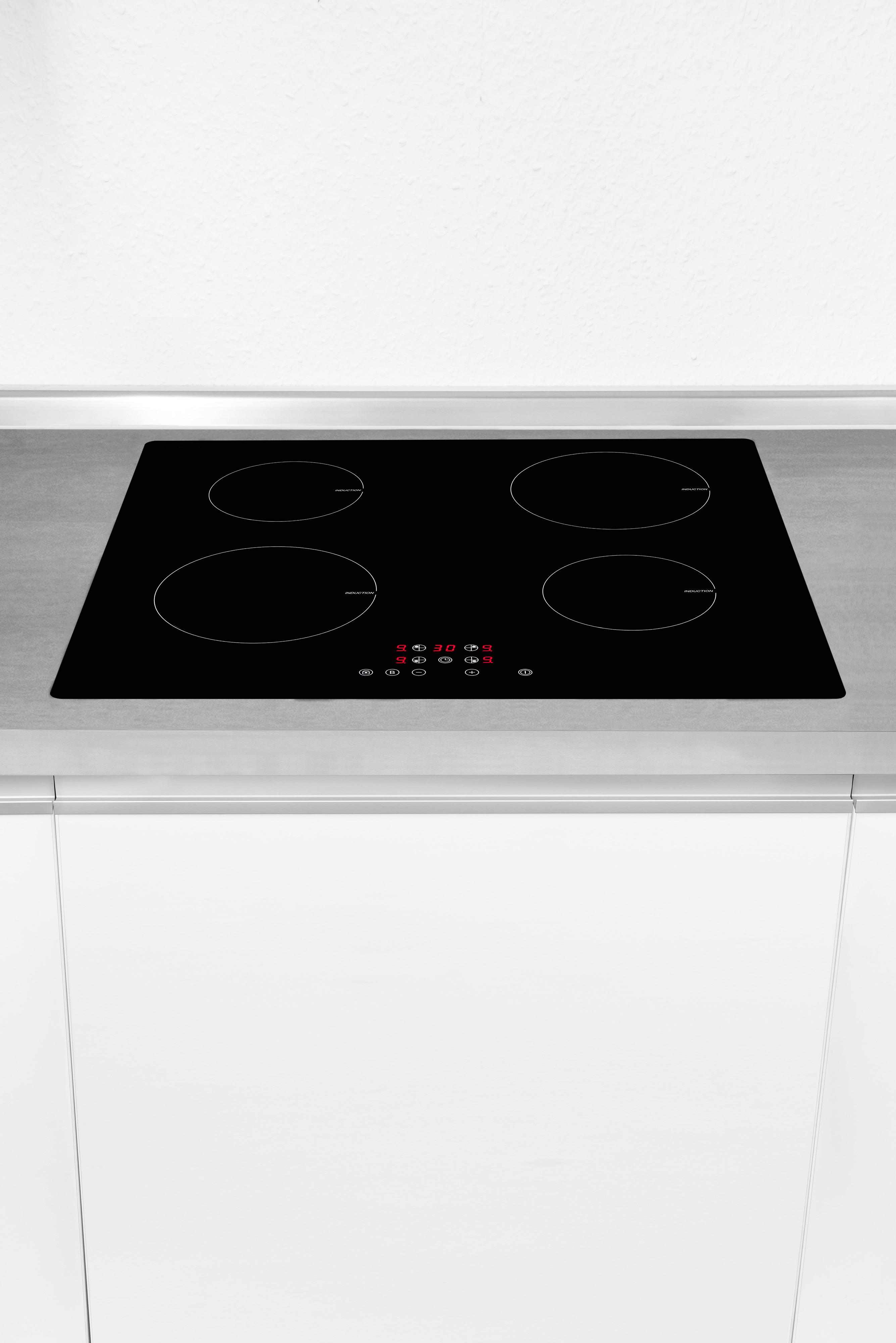Schwarzes Induktionskochfeld auf Metalloberfläche, weißer Schrank.
