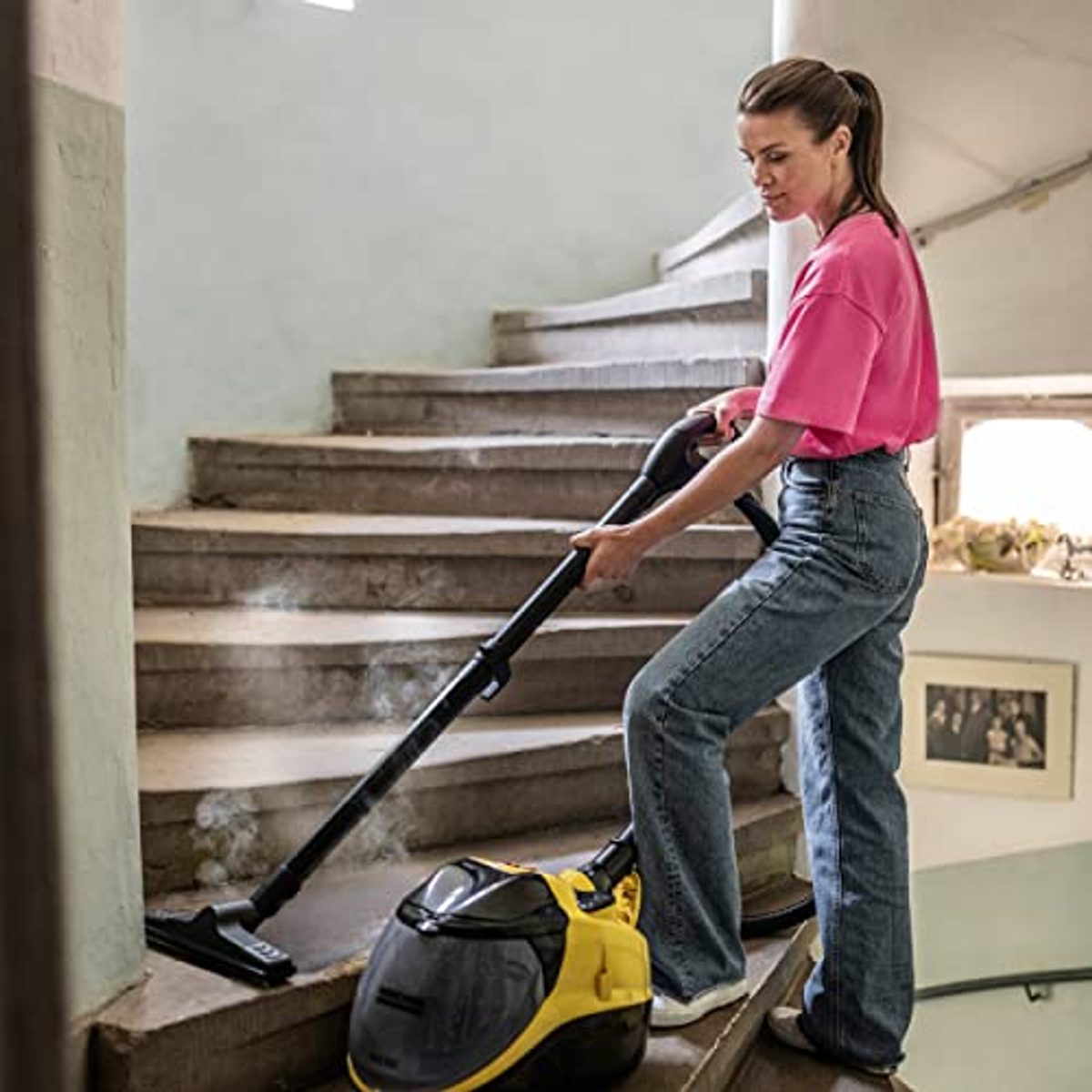 Una donna pulisce le scale con una pulitrice a vapore, in un ambiente domestico.