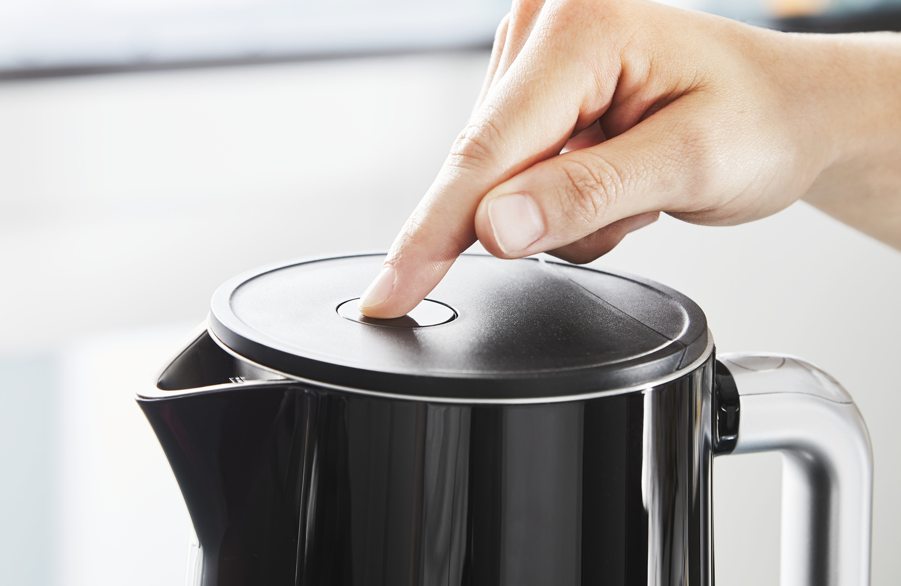 Ręka naciskająca przycisk na czarnym czajniku. Czarny czajnik ze srebrnym dziobkiem.