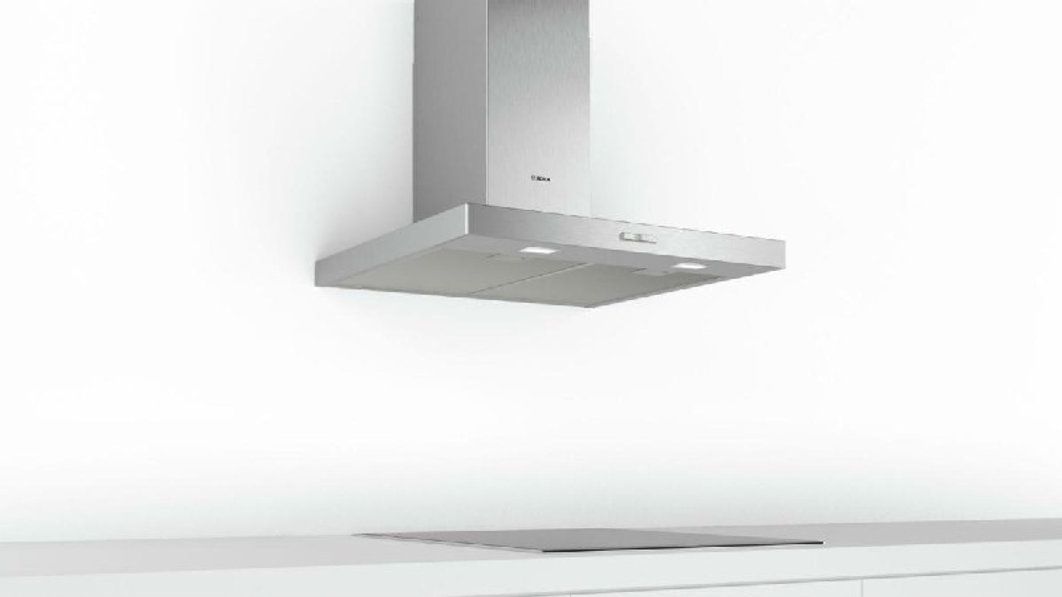 Cappa in acciaio inox montata su parete bianca, sopra piano cottura nero. Due luci sulla cappa.