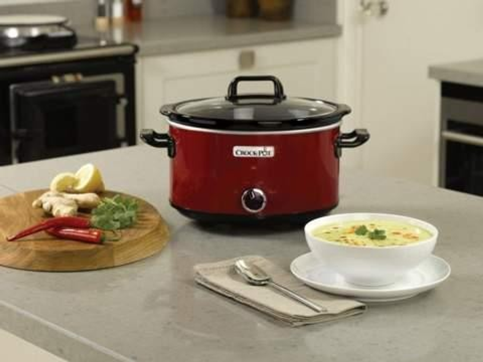 Czerwony wolnowar Crock-Pot z przezroczystą pokrywą, na blacie z jedzeniem.