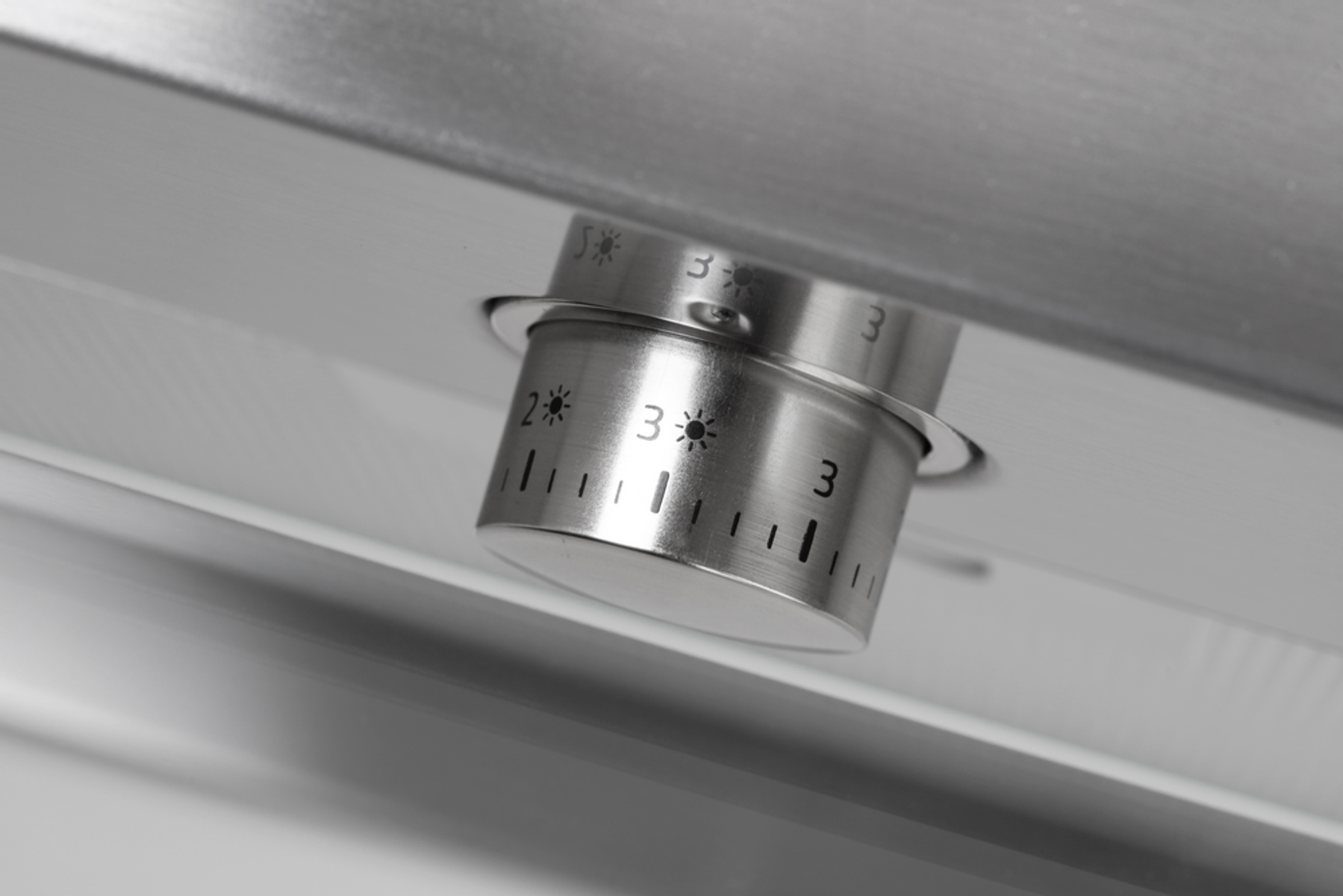 Zbliżenie metalowego pokrętła sterowania z numerami i symbolami na białej powierzchni.