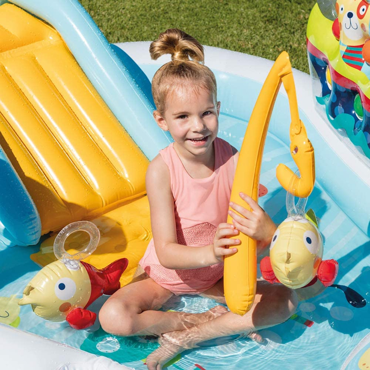 Bambina in piscina con set da pesca giocattolo. Canna e pesce gialli. Giocattoli colorati.