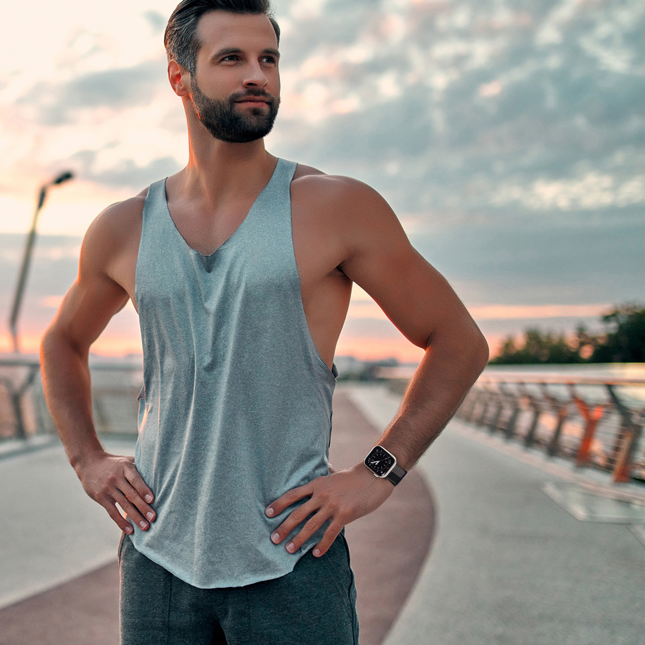 Ein Mann in grauem Tanktop steht auf einer Brücke und trägt eine schwarze Uhr. Der Himmel ist bewölkt.