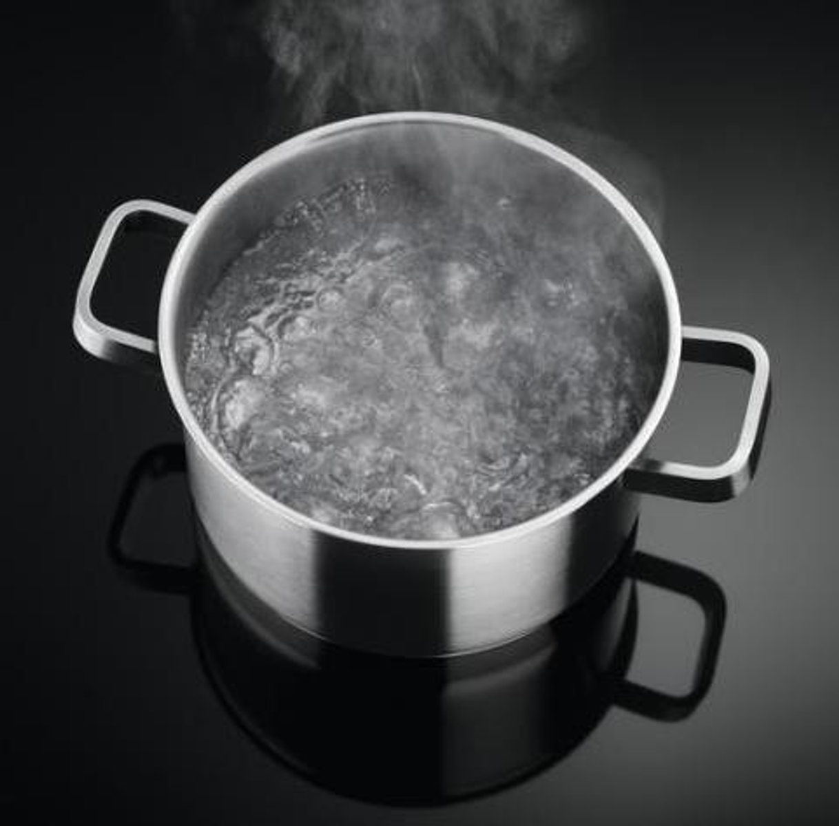 Una olla de acero inoxidable con agua hirviendo y vapor que se eleva de ella.
