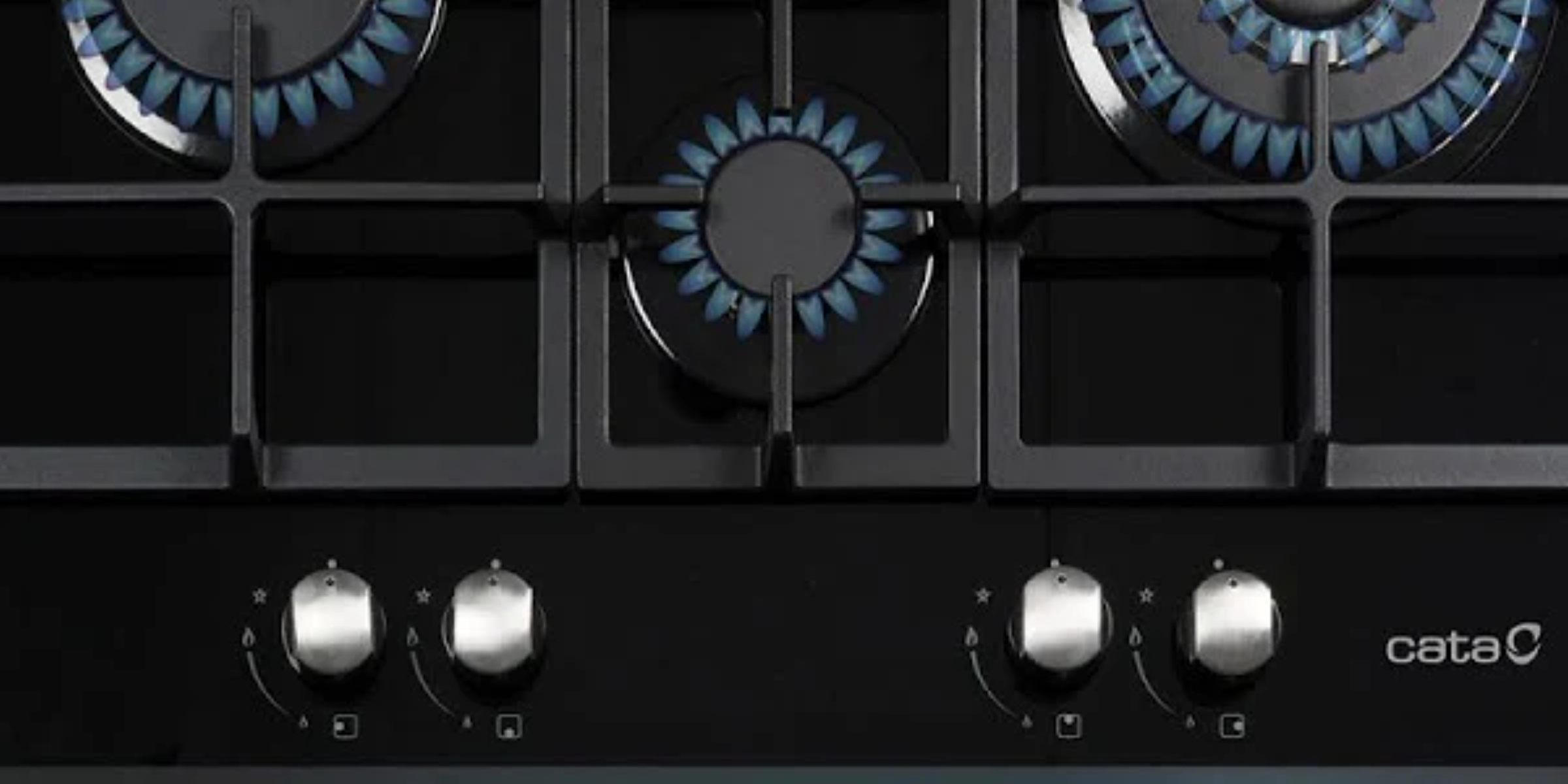 Zbliżenie czarnej płyty grzewczej z trzema palnikami gazowymi. Widoczne niebieskie płomienie.