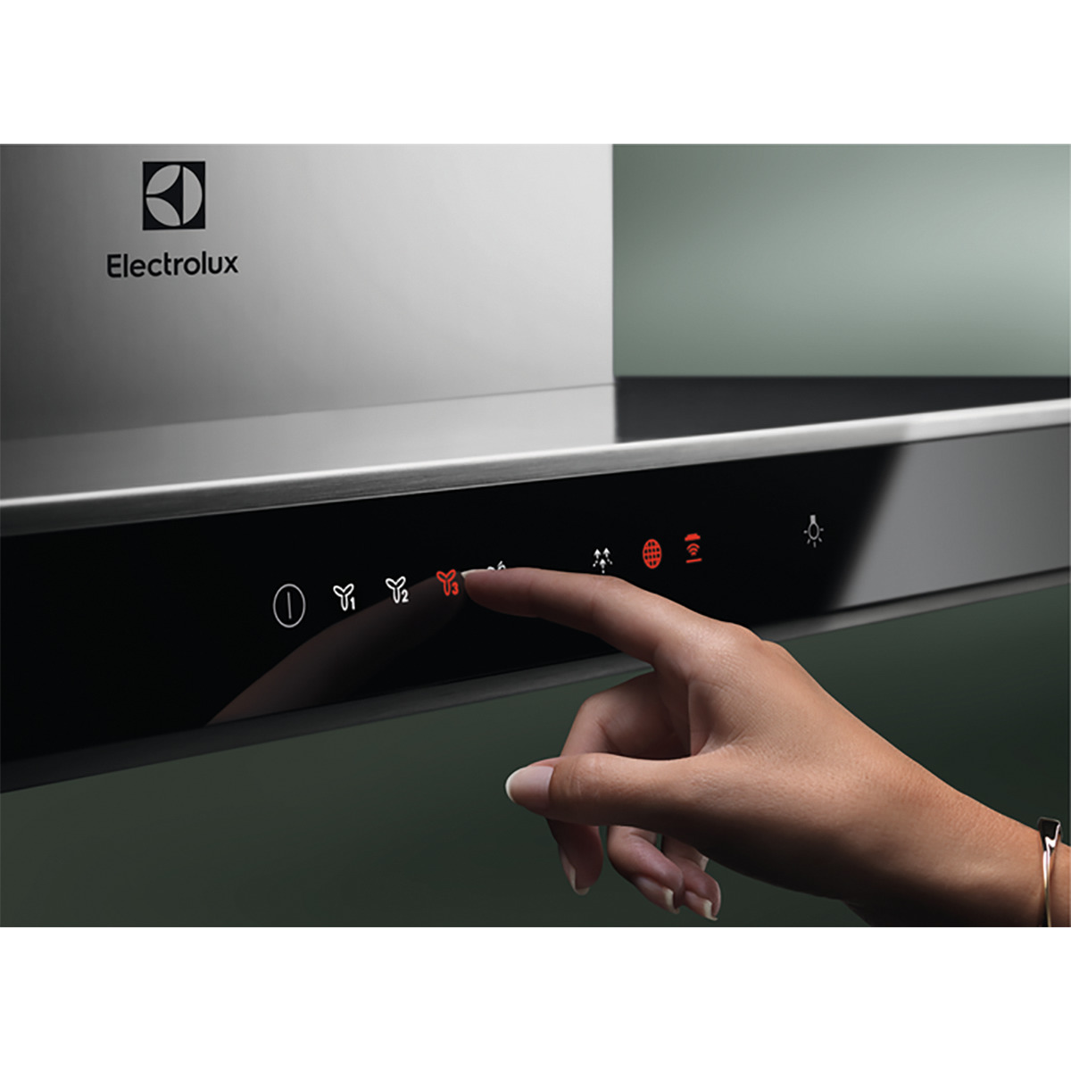 Mano tocando el panel de control de una campana Electrolux negra, fondo verde.