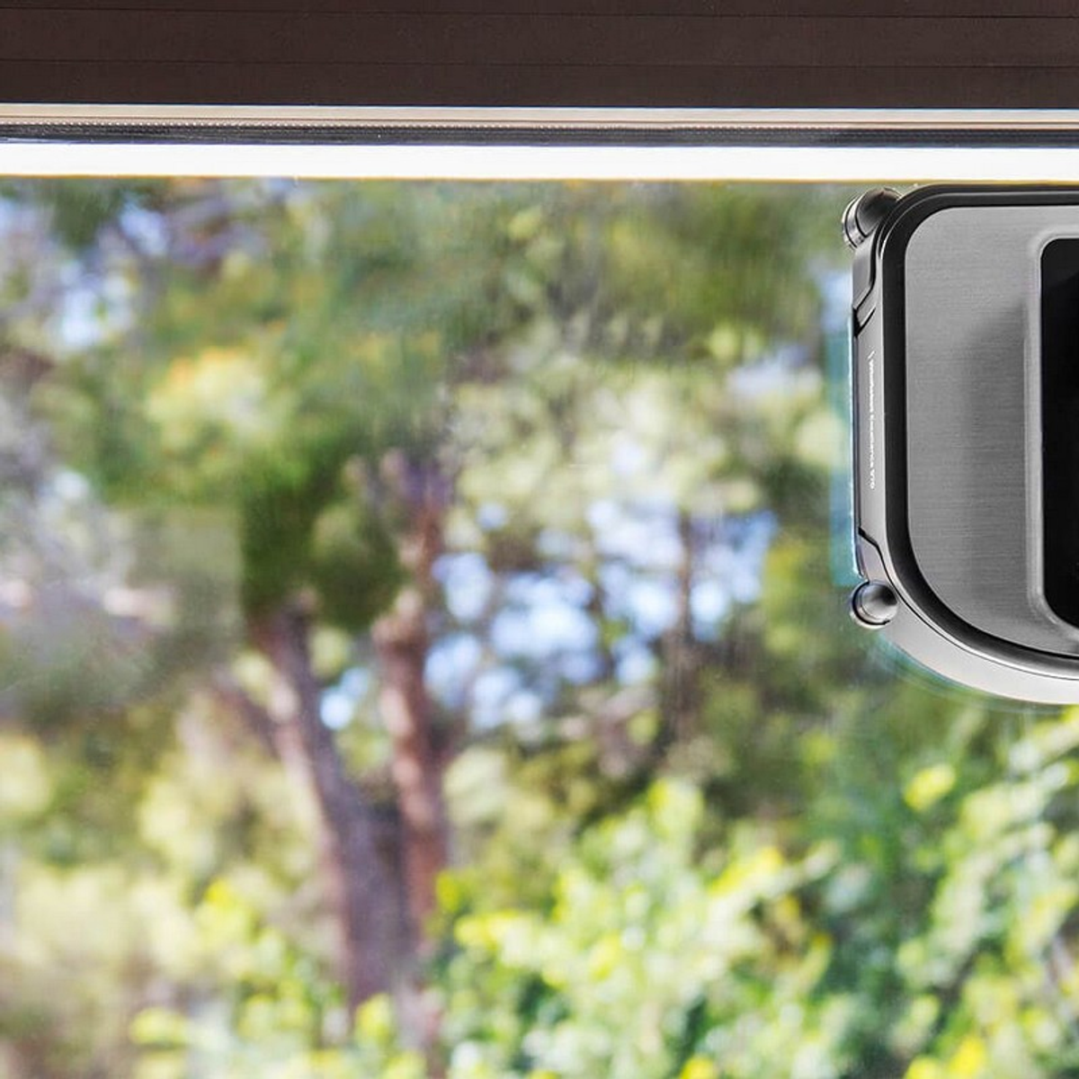 Una ventana con un limpiacristales y un fondo borroso de árboles verdes y cielo.