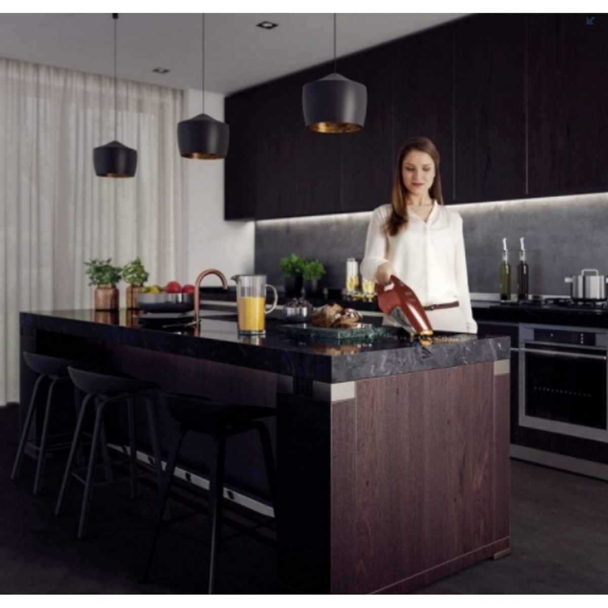 Una mujer aspira migas en una isla de cocina con taburetes. Se ven armarios oscuros y luces colgantes.