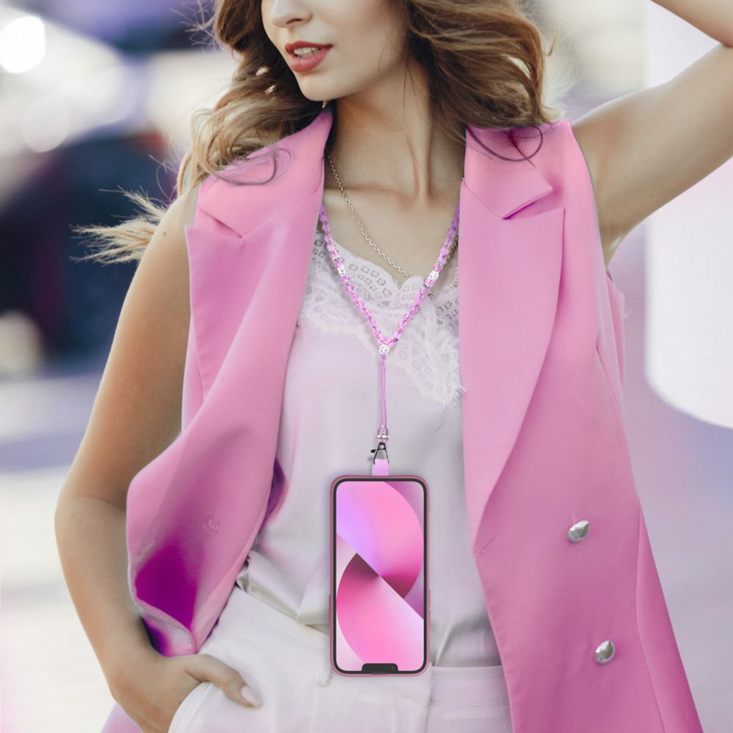 Frau trägt rosa Blazer und Halskette, hält Handy mit rosa Hülle, Nahaufnahme.