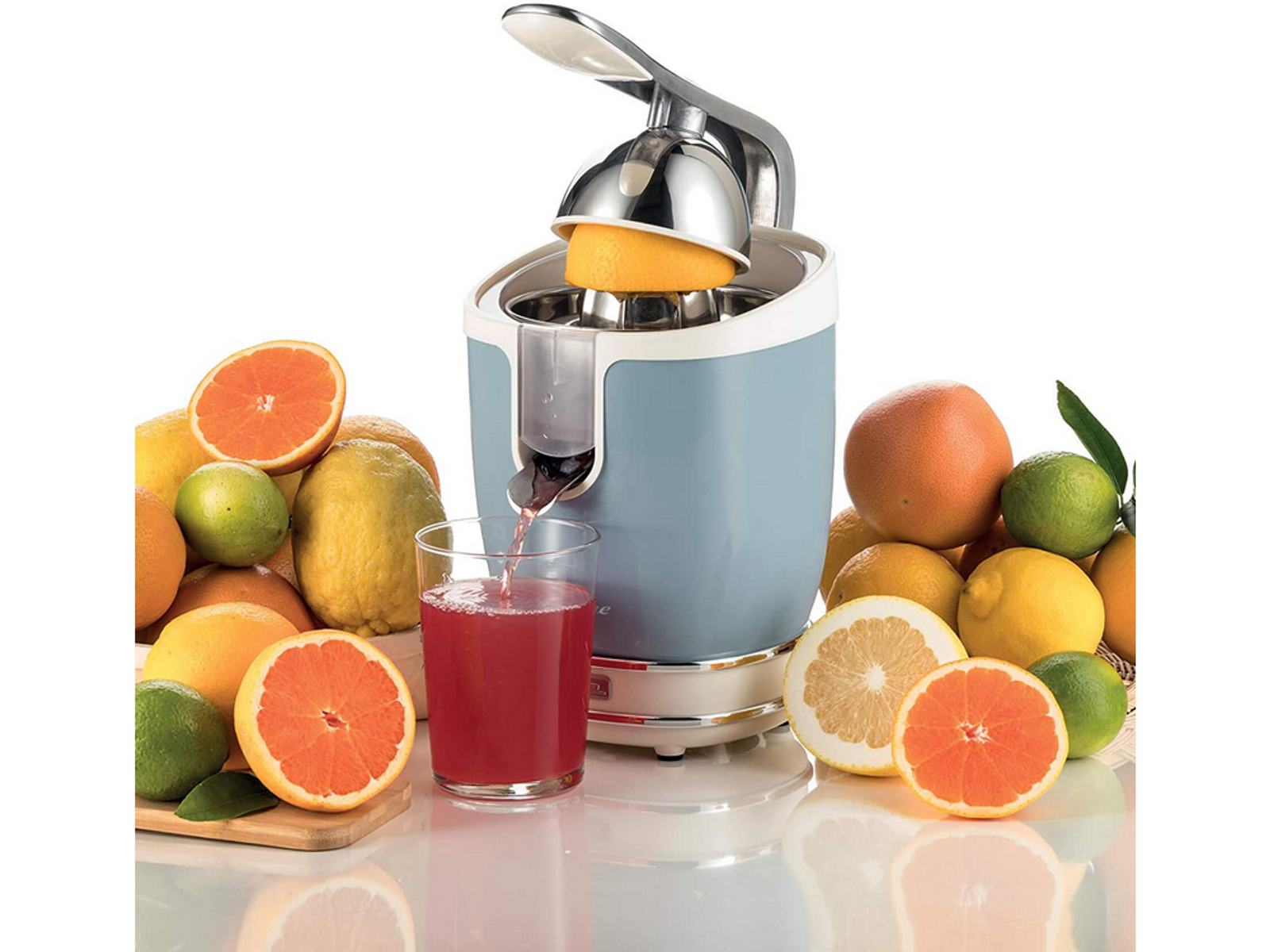 Ein Entsafter presst eine Grapefruit. Weitere Zitrusfrüchte und ein Glas Saft sind im Bild.