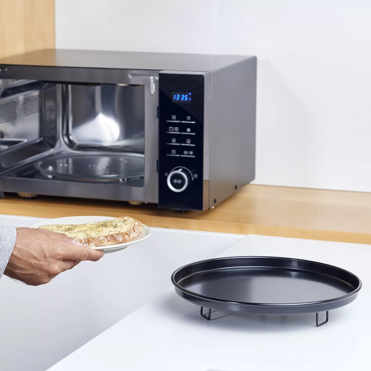 Un forno a microonde con un piatto di cibo davanti e un vassoio sul bancone.