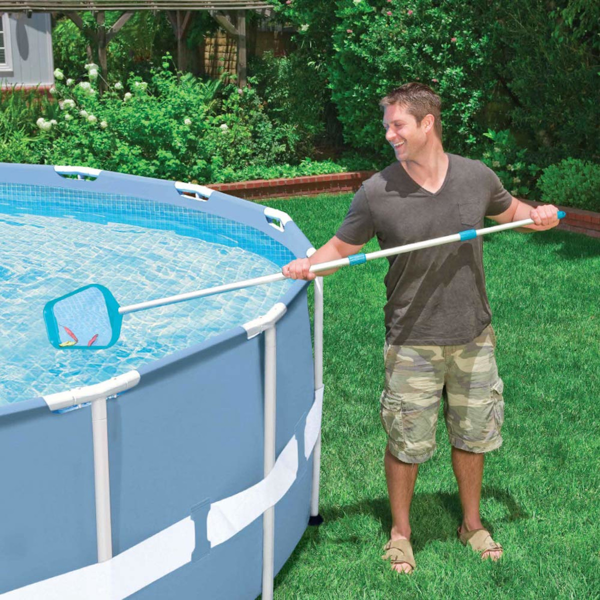 Homme nettoyant une piscine avec un filet. Piscine bleue, herbe verte.