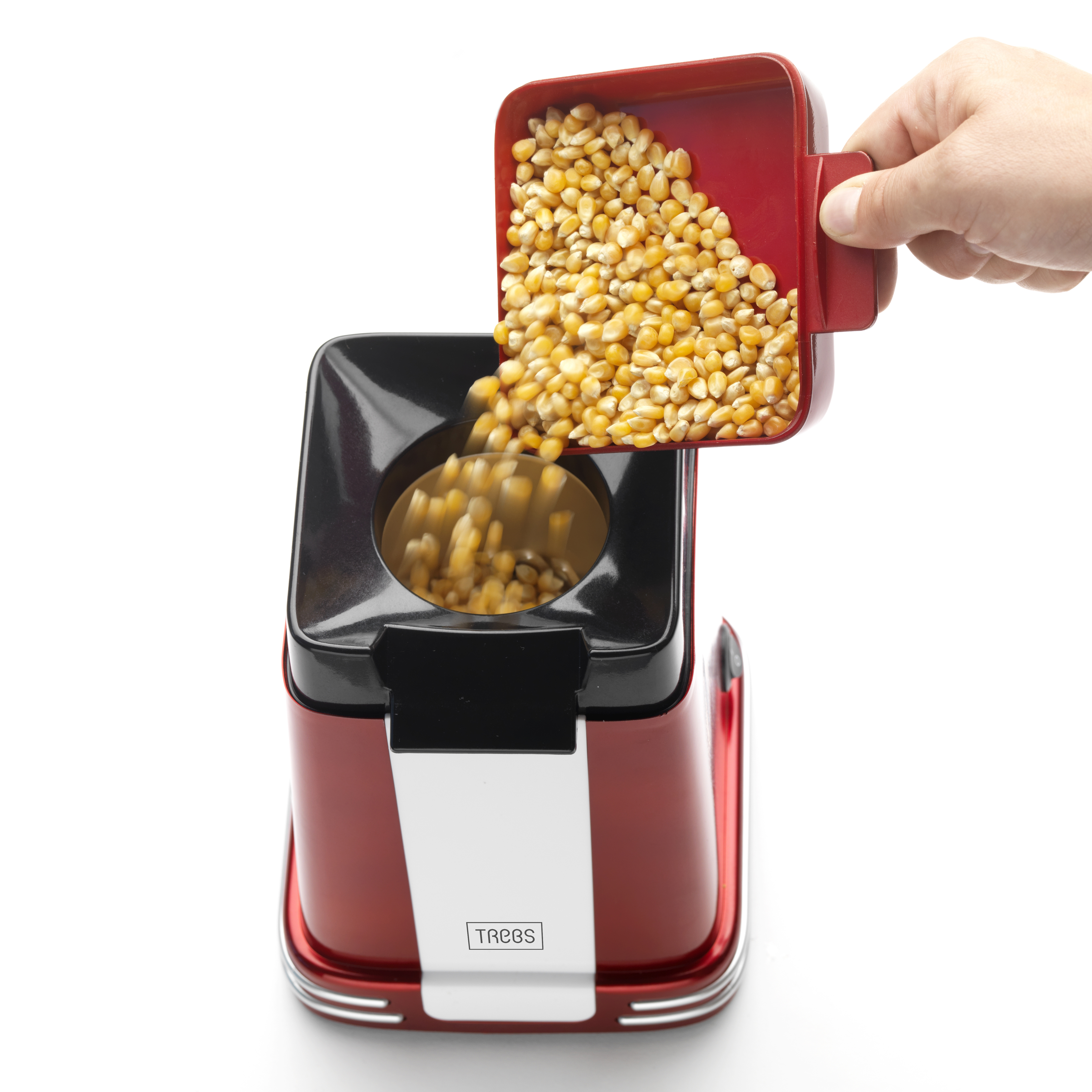 Ein roter Popcornbereiter mit Maiskörnern, die aus einem roten Löffel, der von einer Hand gehalten wird, hineingegossen werden.