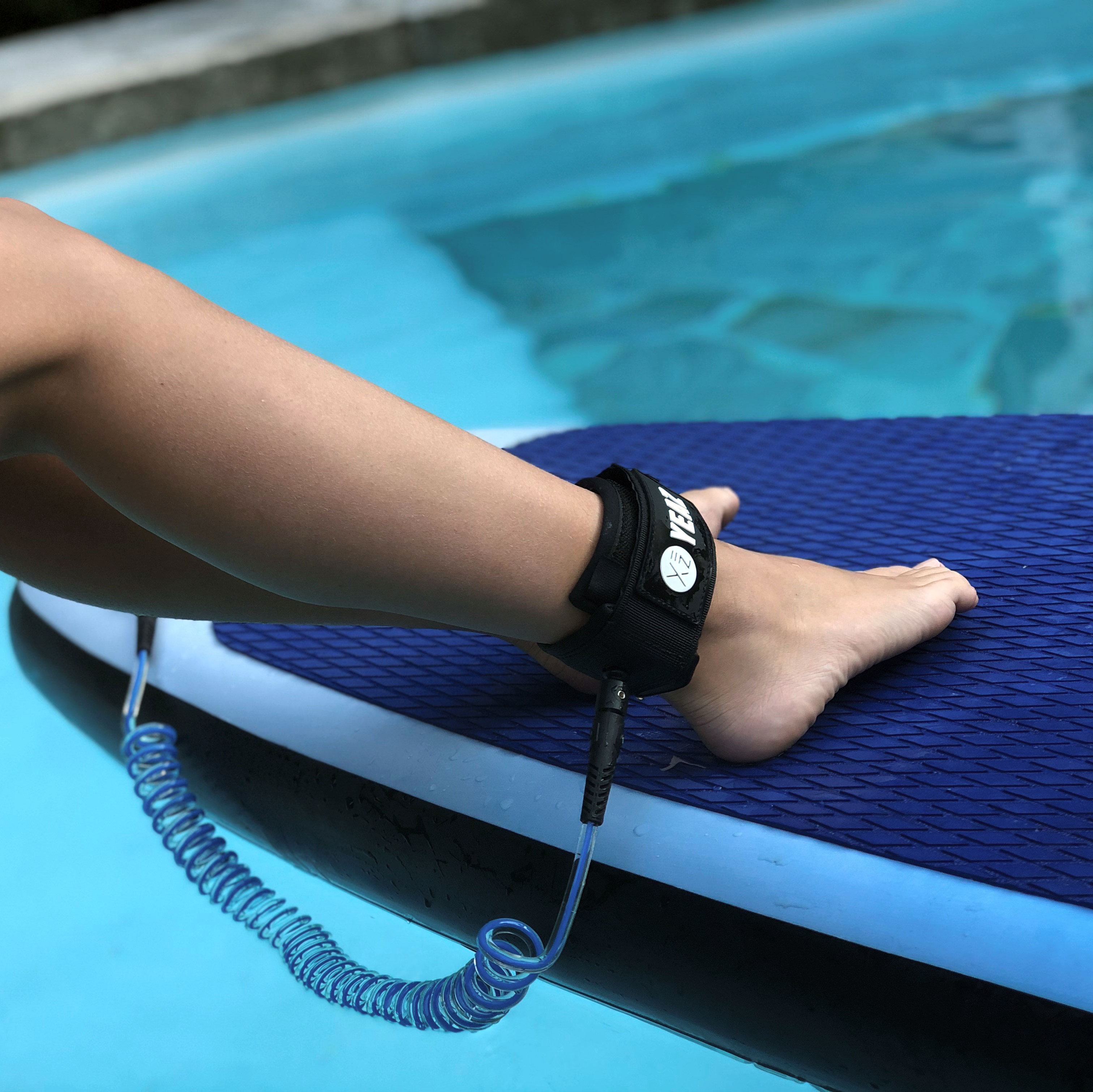 Personenfüße mit einer Leine, die an einem Paddleboard befestigt ist, bereit für Wasseraktivitäten.