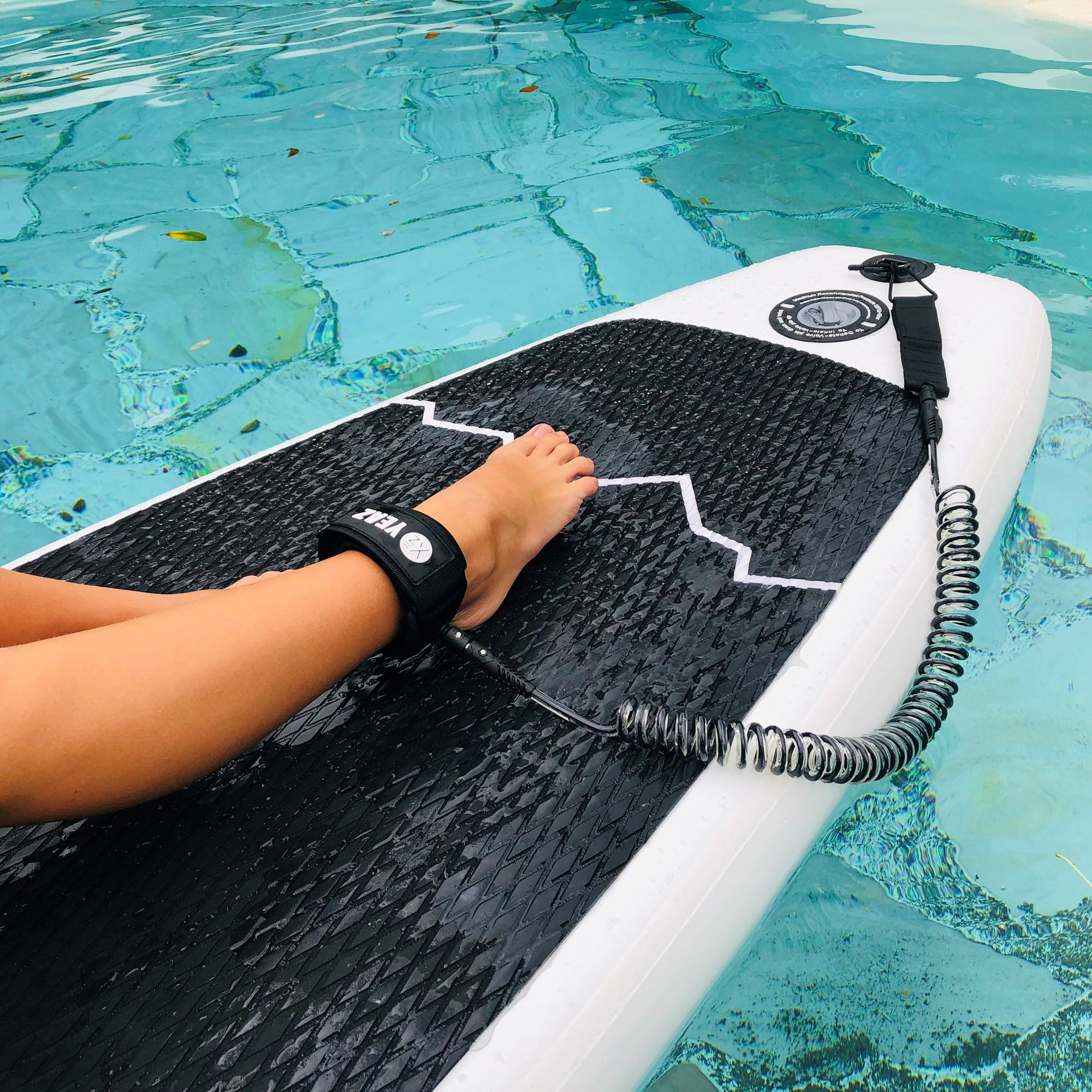 Die Füße einer Person auf einem weiß-schwarzen Paddleboard in einem Pool.