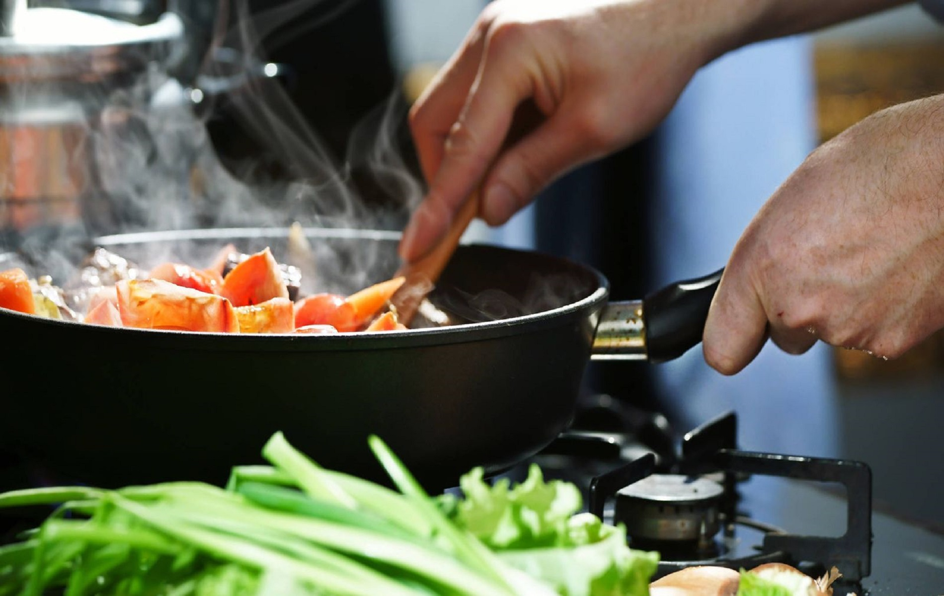 Una persona cocinando comida en una sartén en una estufa, con verduras en primer plano.