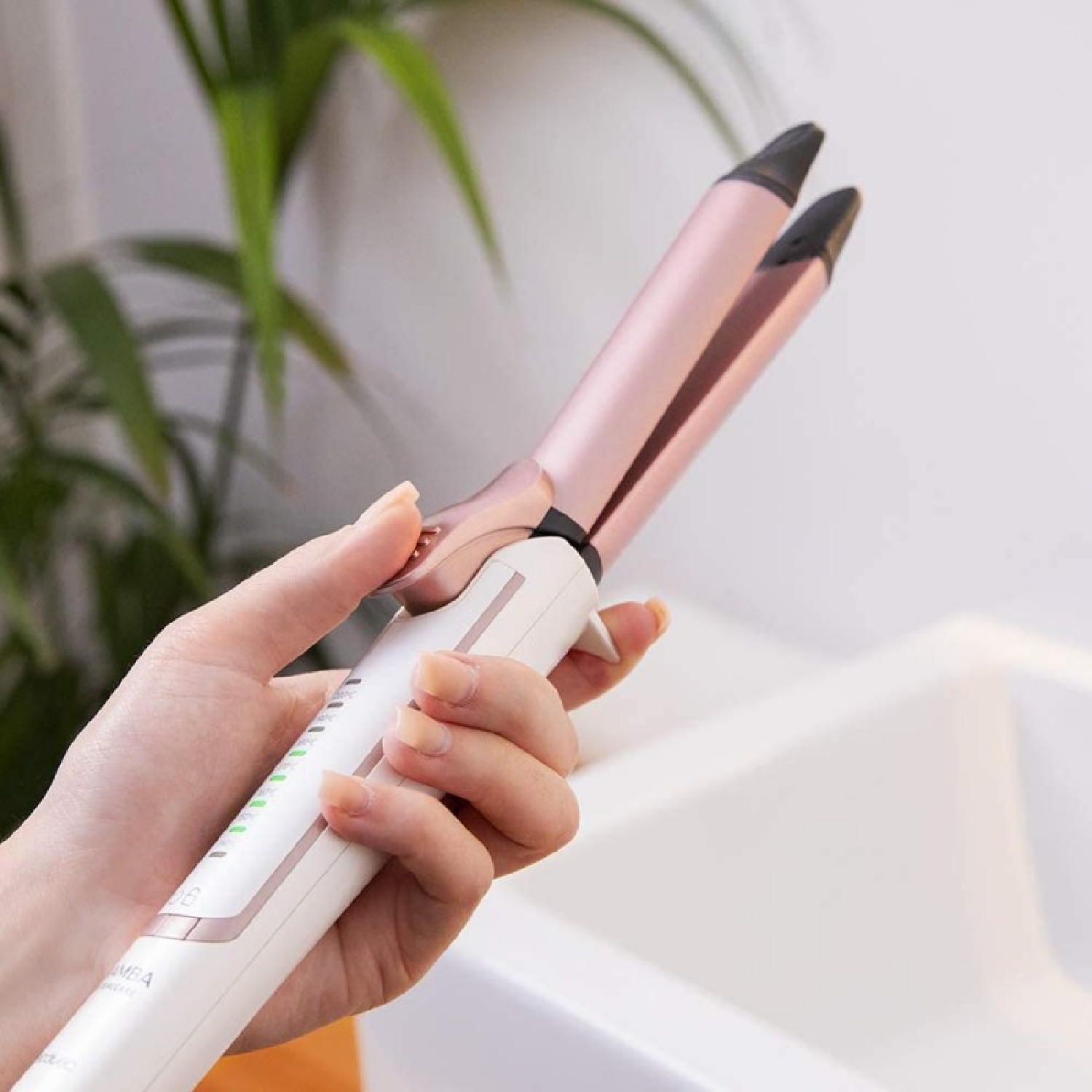 Dłoń trzyma lokówkę w kolorze różowego złota i bieli z zielonymi lampkami kontrolnymi.