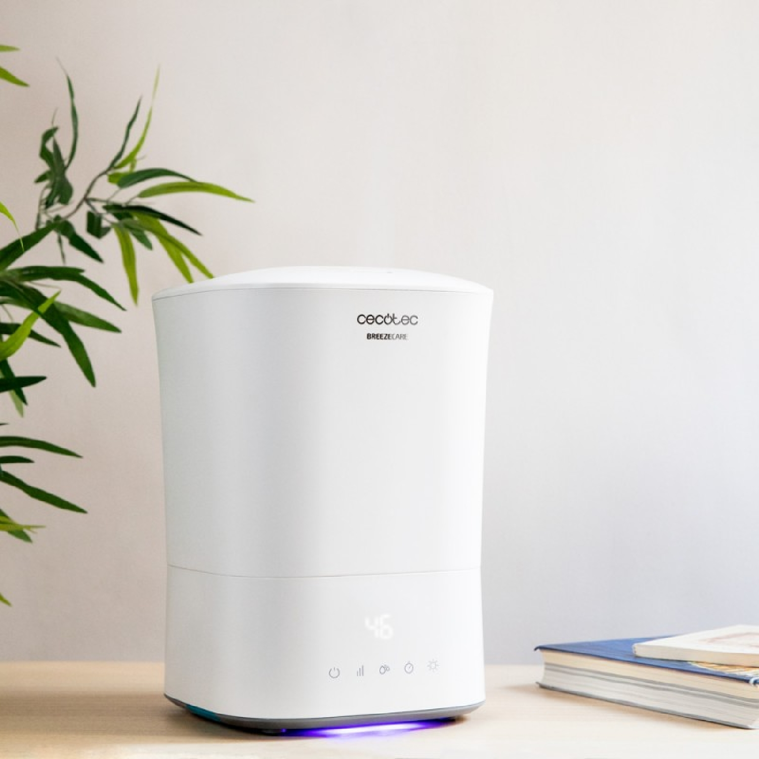 Umidificatore d'aria bianco con display. Libri e pianta sullo sfondo.