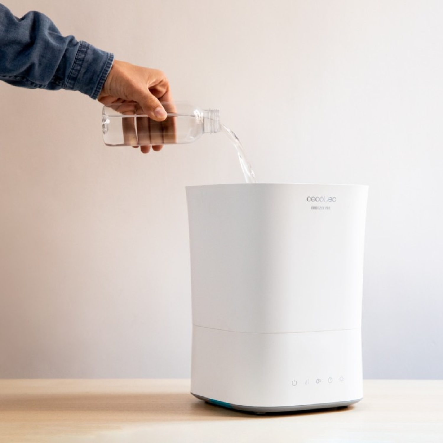 Una persona versa acqua da una bottiglia in un umidificatore bianco.